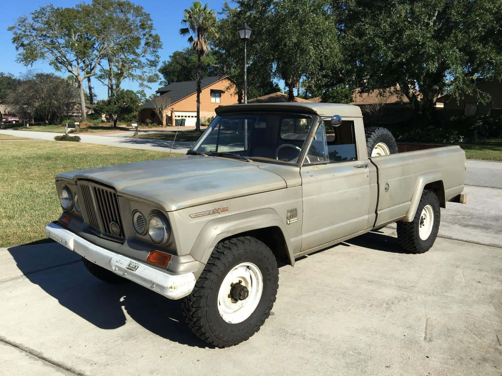Jeep Gladiator 桌布 壁紙 — 一輛復古米色Jeep皮卡車，配備白色側壁輪胎，停在混凝土車道上，天空湛藍。