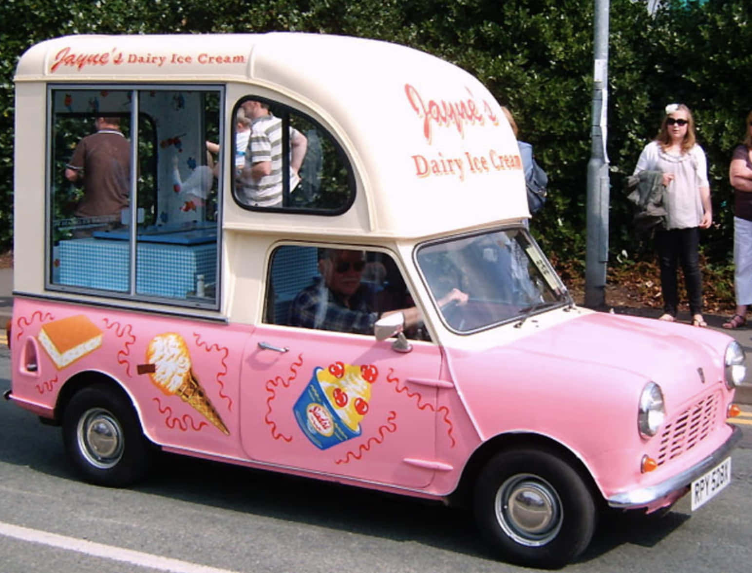 Ice Cream Truck 桌布 壁紙 — 一輛復古粉紅色冰淇淋車，帶有卡通冰淇淋圖案，停在陽光明媚的街道上，附近有人。