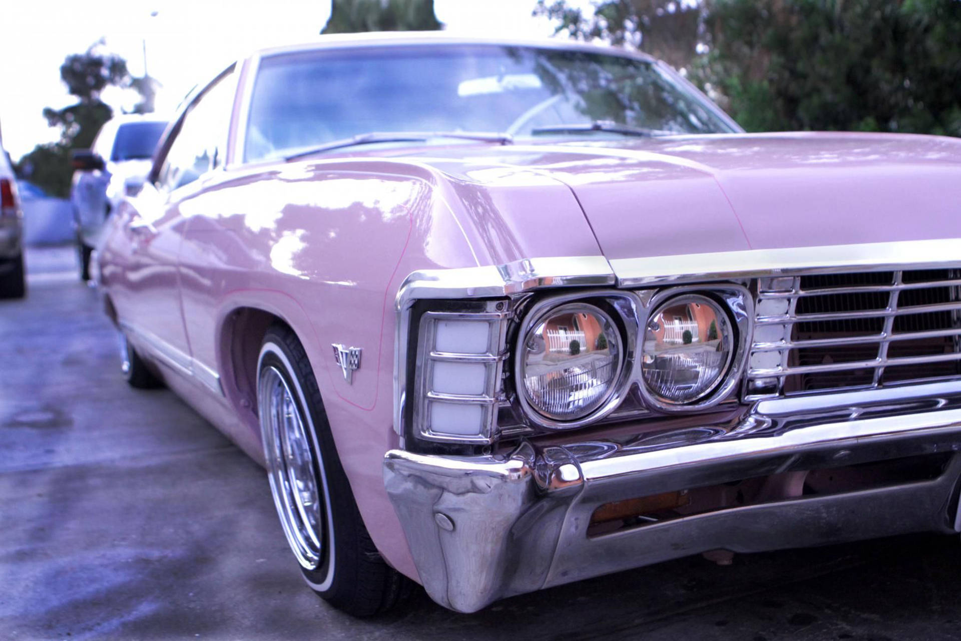 chevrolet impala 1967 桌布 壁紙 — 一輛復古粉紅色肌肉車，帶有鍍鉻細節，在停車場的柔和日光下閃閃發光。
