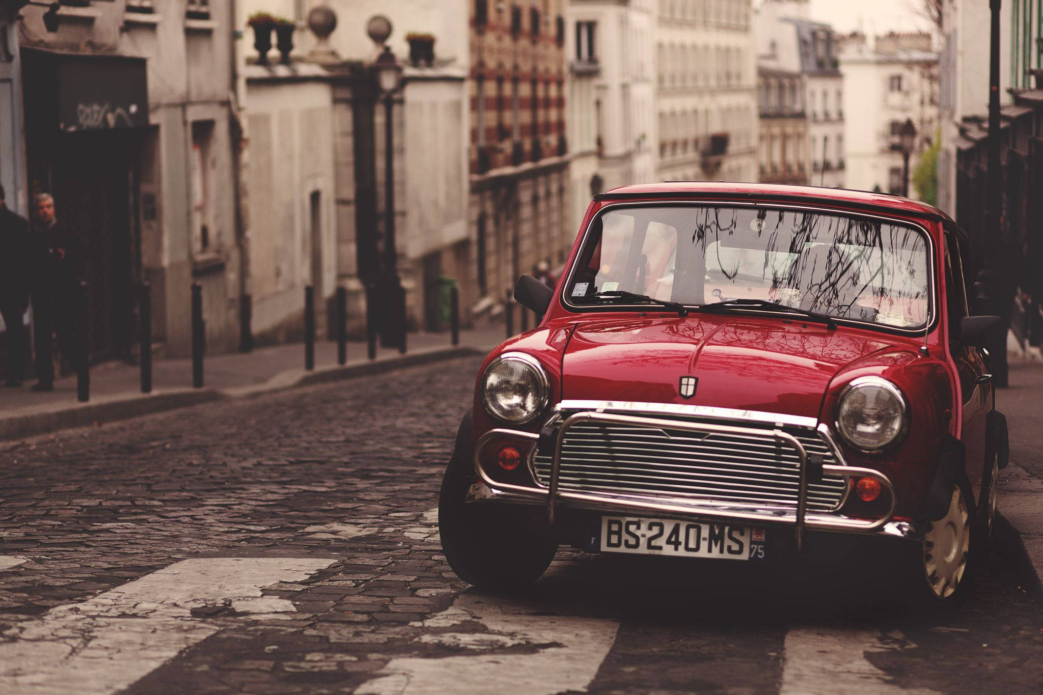 Mini Cooper 桌布 壁紙 — 一輛復古紅色Mini Cooper停在歐洲城市的鵝卵石街道上，背景是模糊的歷史建築。