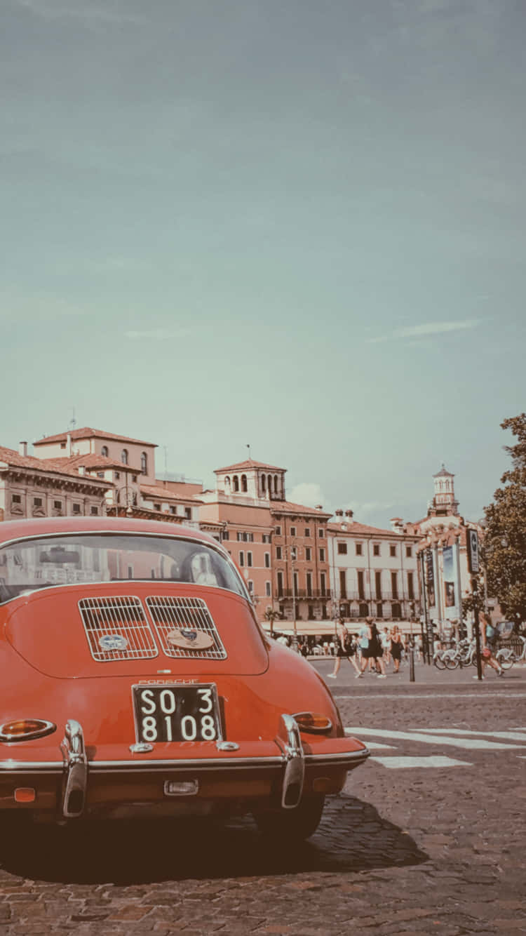 Italy Aesthetic 桌布 壁紙 — 一輛復古紅色保時捷356停在鵝卵石街道上，背景是歷史悠久的歐洲建築和行人。