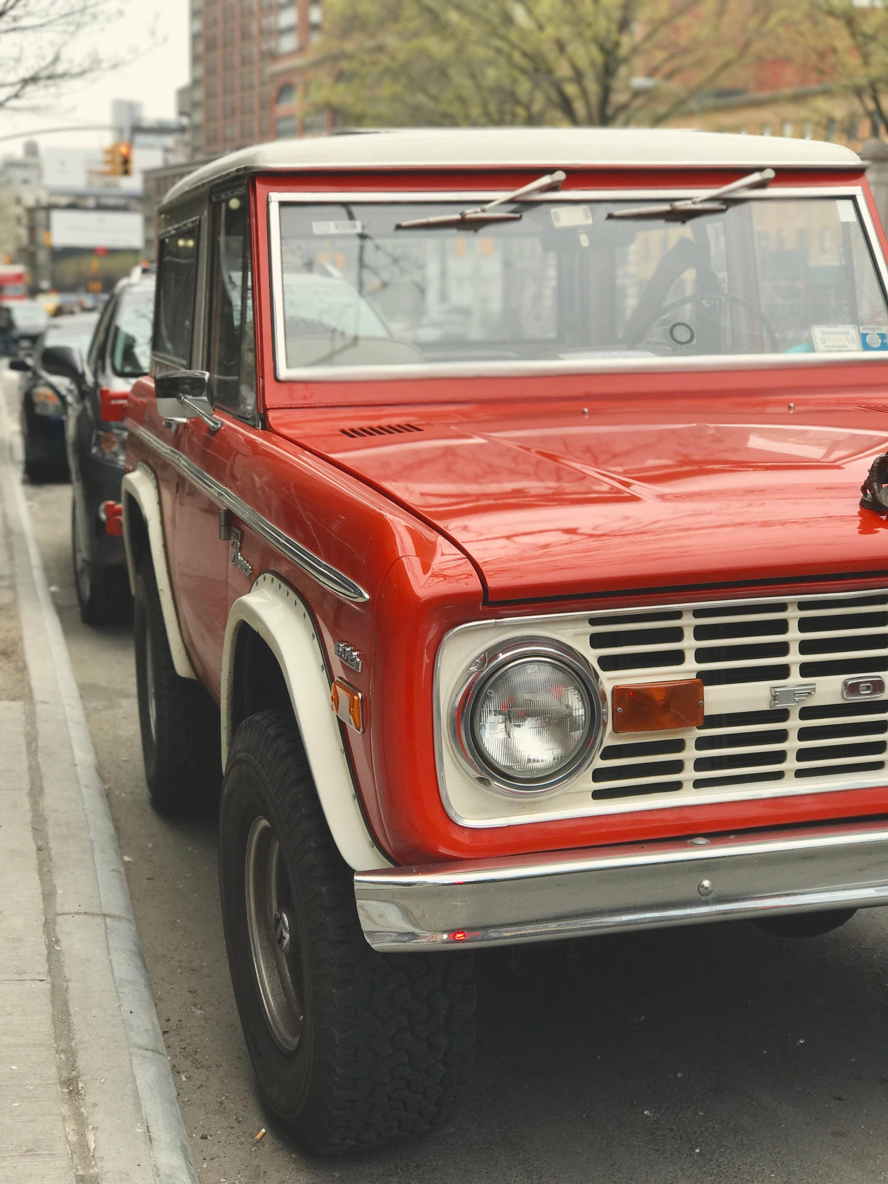 Ford Bronco 桌布 壁紙 — 一輛復古紅色和白色的福特Bronco停放在城市街道上，背景有光禿禿的樹木和城市建築。
