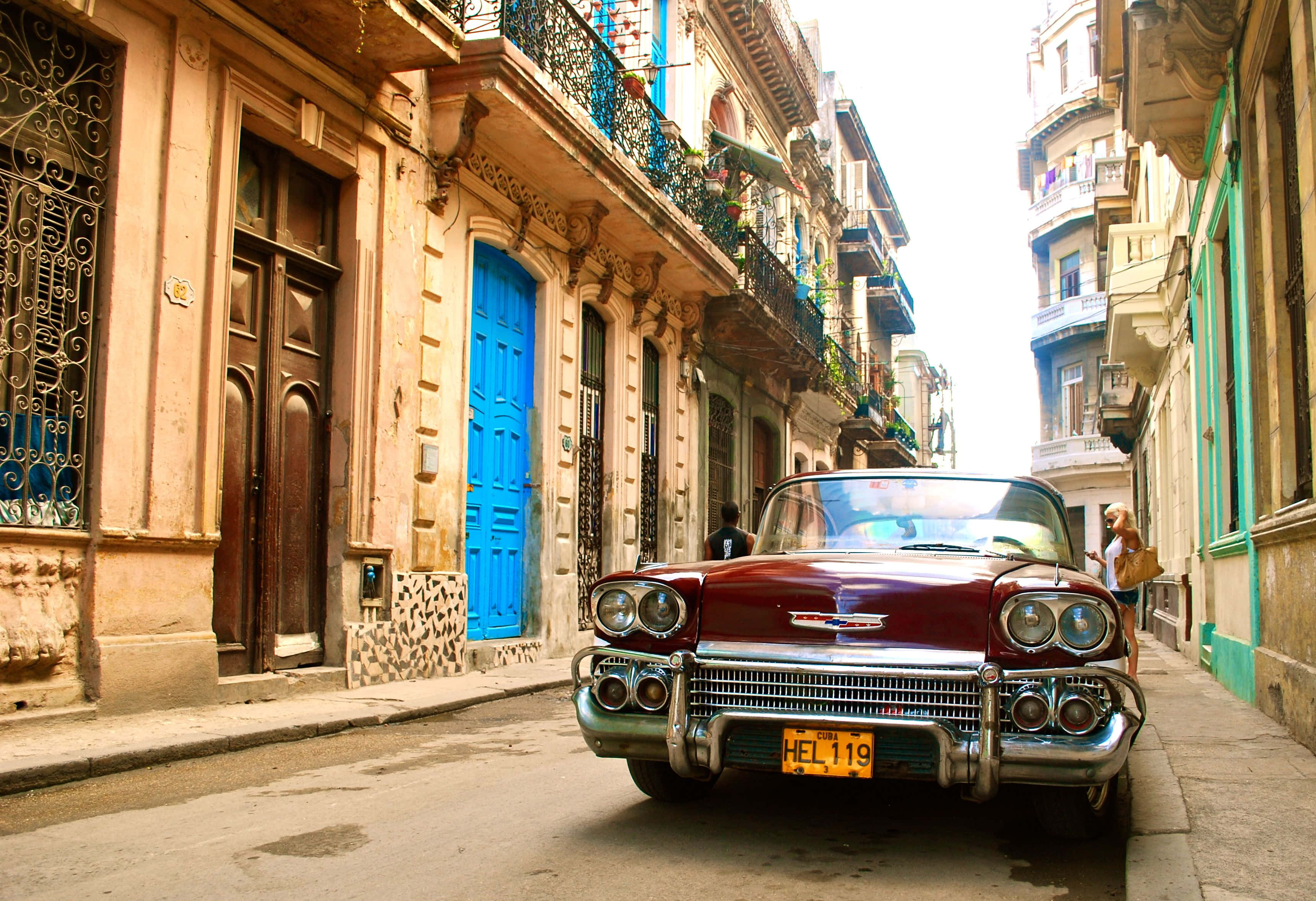 Cuba 桌布 壁紙 — 一輛復古紅色敞篷車停在陽光明媚的哈瓦那街道上，兩旁是色彩繽紛的殖民時期建築和鐵藝陽台。