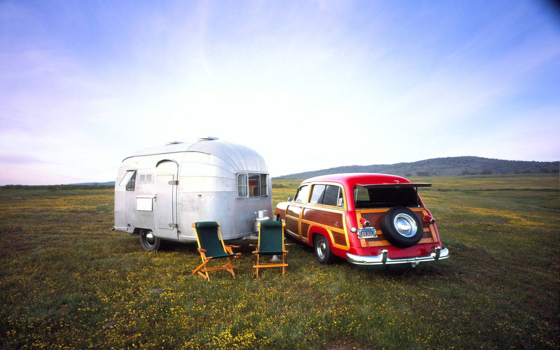 Camping 桌布 壁紙 — 一輛復古紅色木紋旅行車和銀色Airstream露營車停泊在黃昏時分陽光明媚的黃色野花田裡。