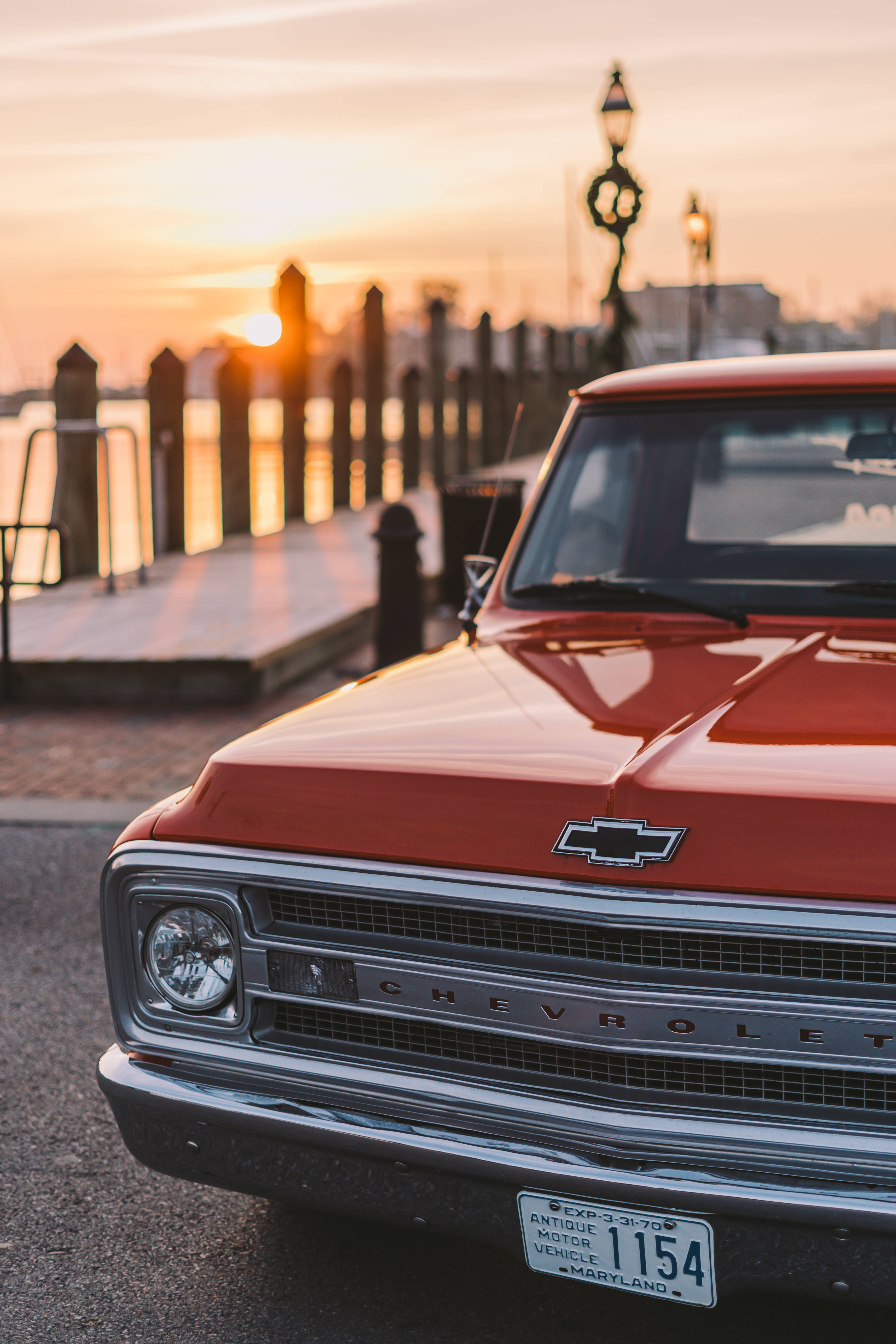 Chevrolet 桌布 壁紙 — 一輛復古紅色雪佛蘭卡車在金色夕陽下閃閃發光，旁邊是海濱碼頭，街燈閃爍。