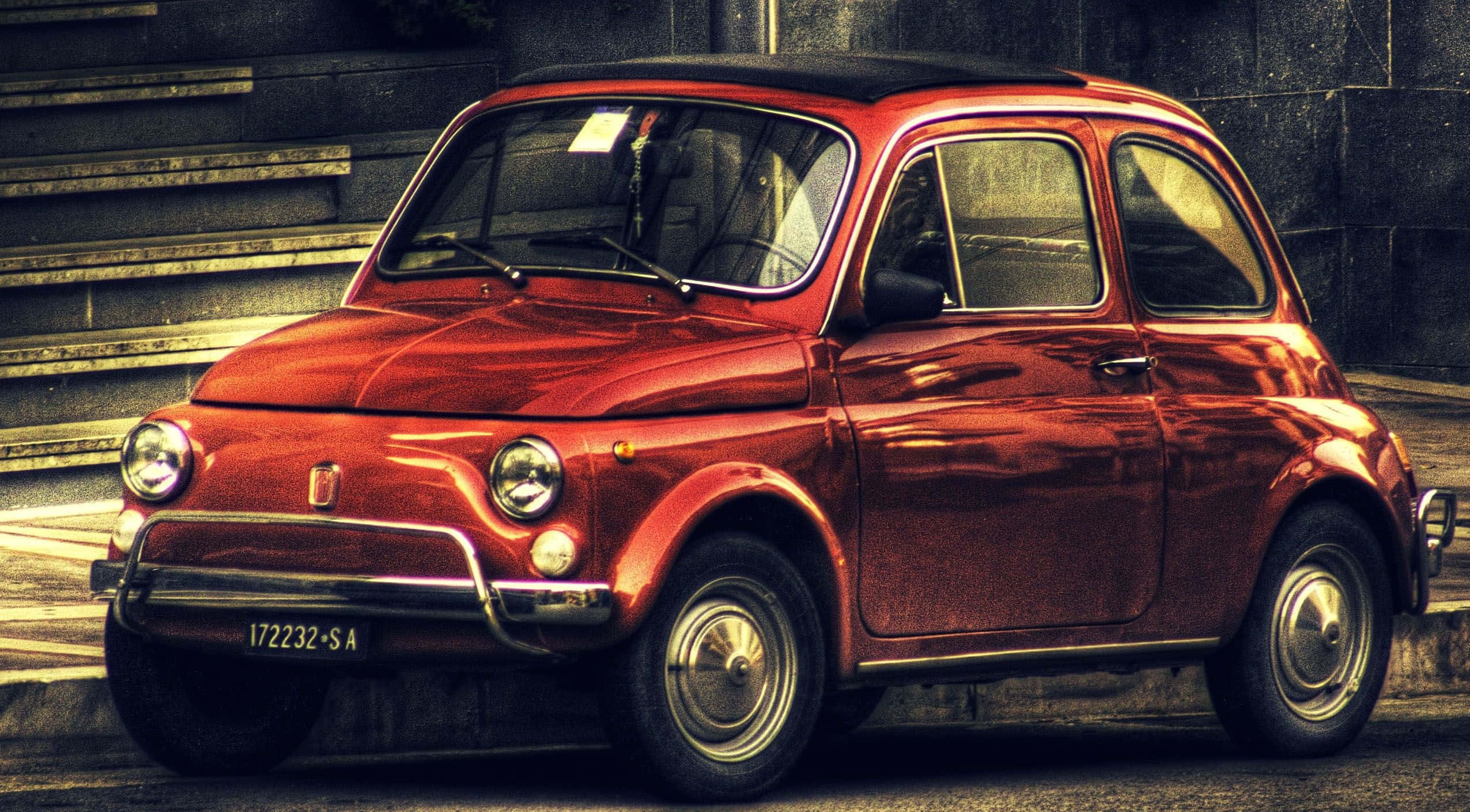 Fiat 500l 桌布 壁紙 — 一輛復古紅色飛雅特500停泊在陽光普照的城市街道上，後面有石階。