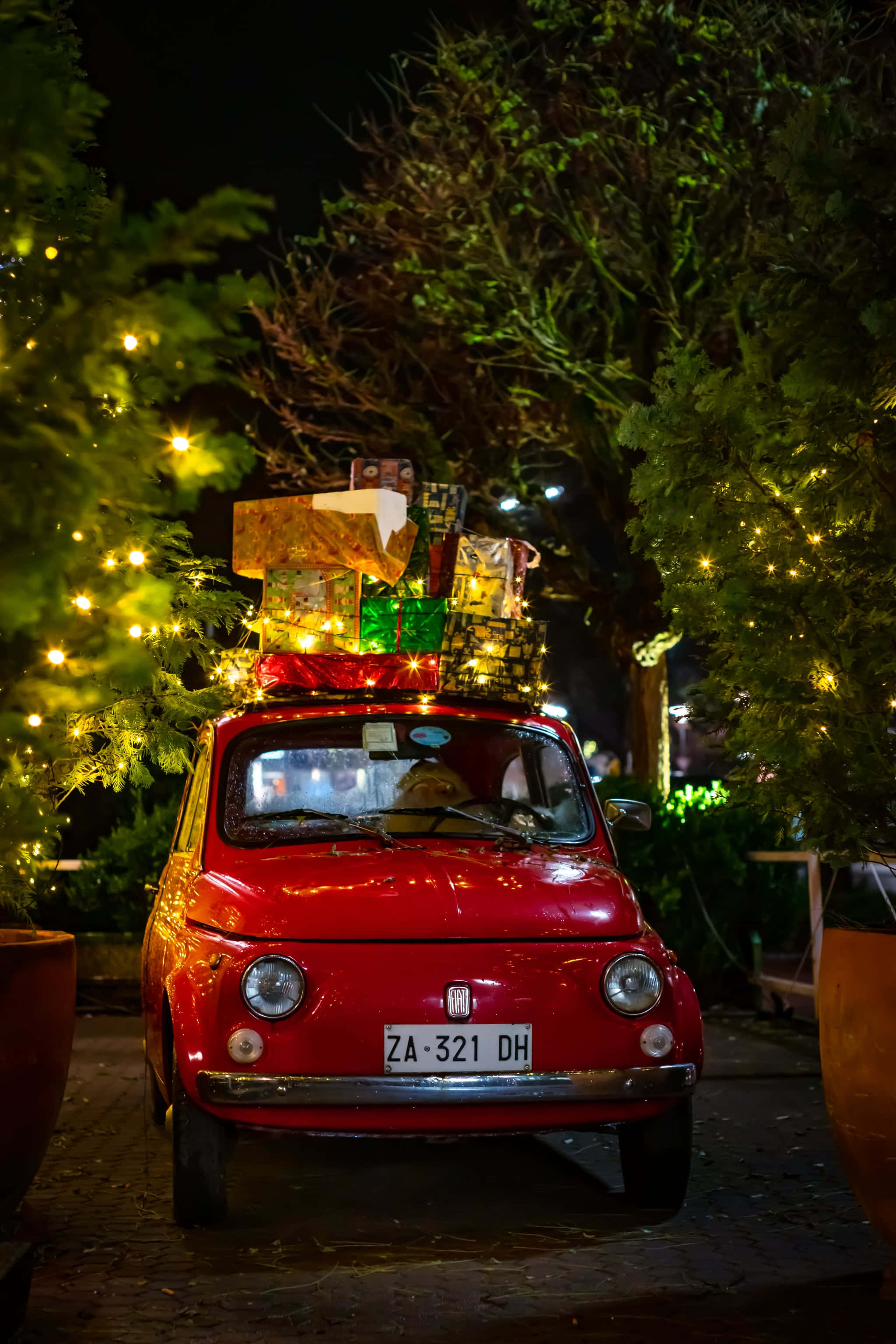 Santa Claus 桌布 壁紙 — 一輛復古紅色飛雅特500在夜晚，在燈串下堆滿了色彩繽紛的聖誕禮物。