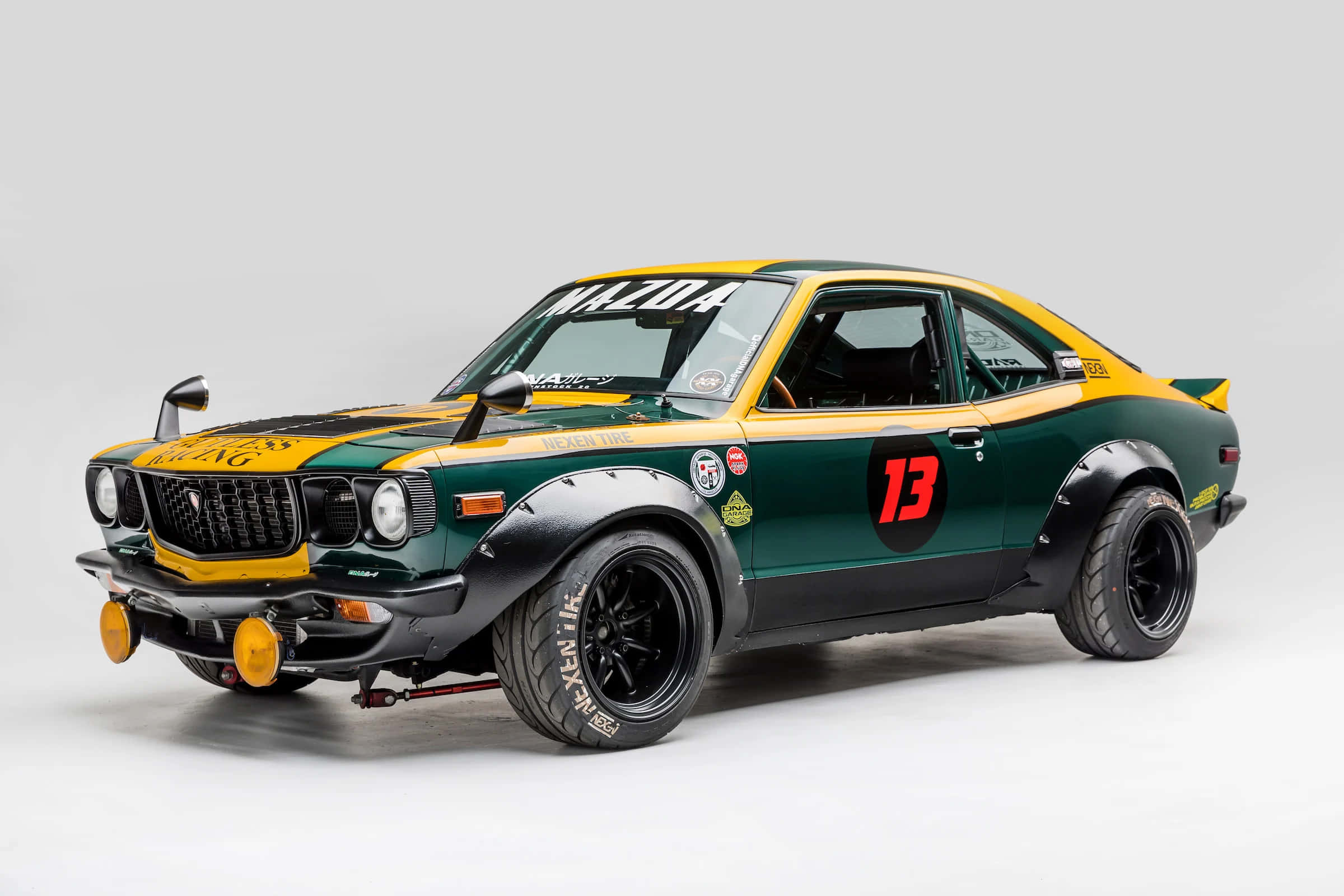 Mazda Rx-3 桌布 壁紙 — 一輛復古綠色和黃色的馬自達RX-3拉力賽車，帶有13號和賽車貼紙，擺放在純白色背景前。