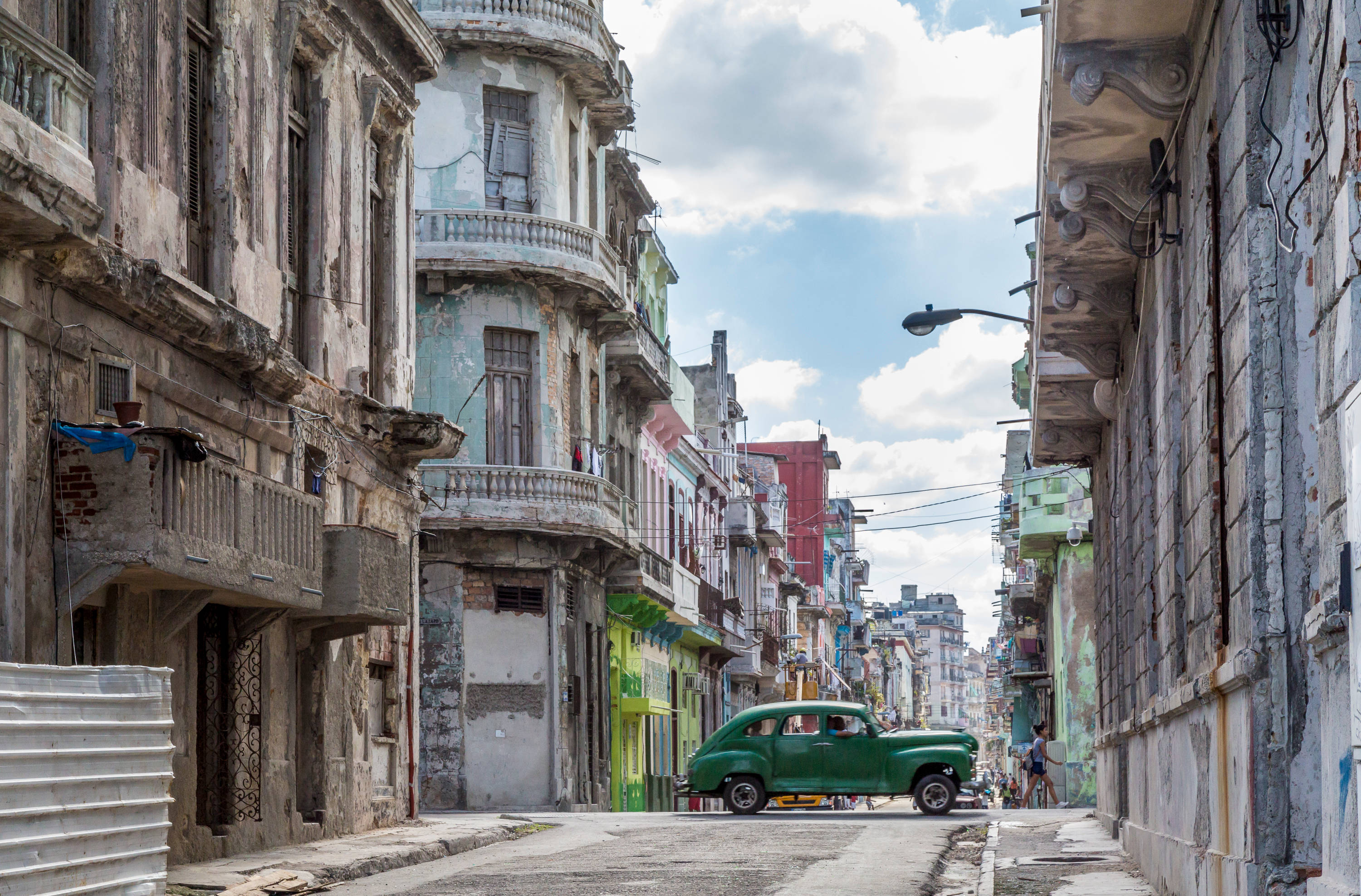 Cuba 桌布 壁紙 — 一輛復古綠色汽車在晴朗藍天下，行駛在一條兩旁盡是飽經風霜的殖民時期建築的狹窄街道上。