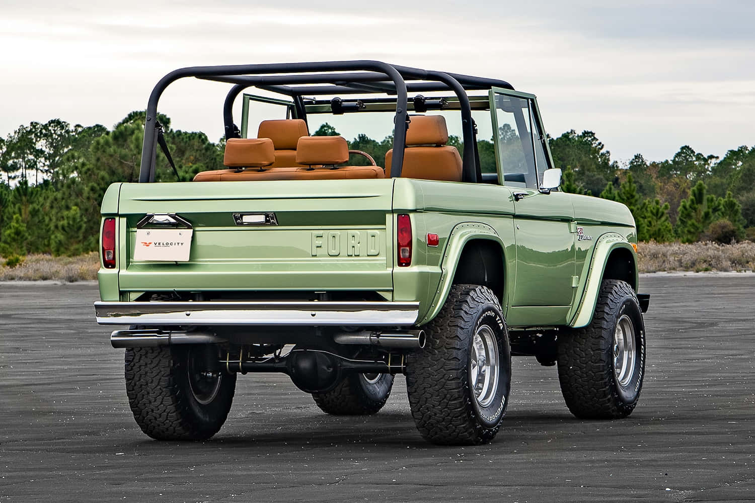 福特野馬越野車 桌布 壁紙 — 一輛復古綠色福特Bronco，配有棕褐色座椅和黑色防滾架，停在瀝青路面上，背景有樹木。