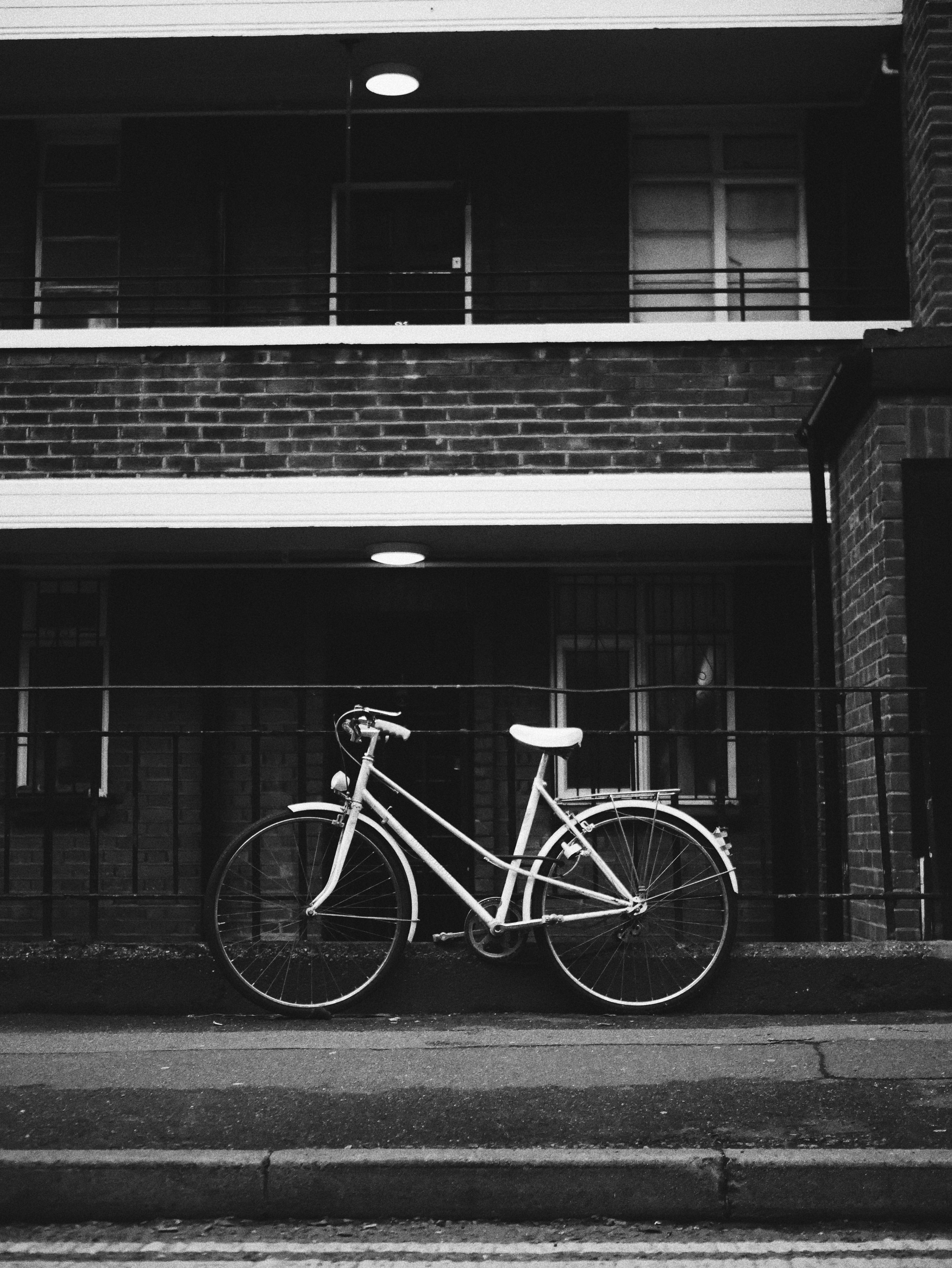 腳踏車 桌布 壁紙 — 一輛復古腳踏車靠在磚造建築上，在柔和頭頂燈光下的單色城市場景。