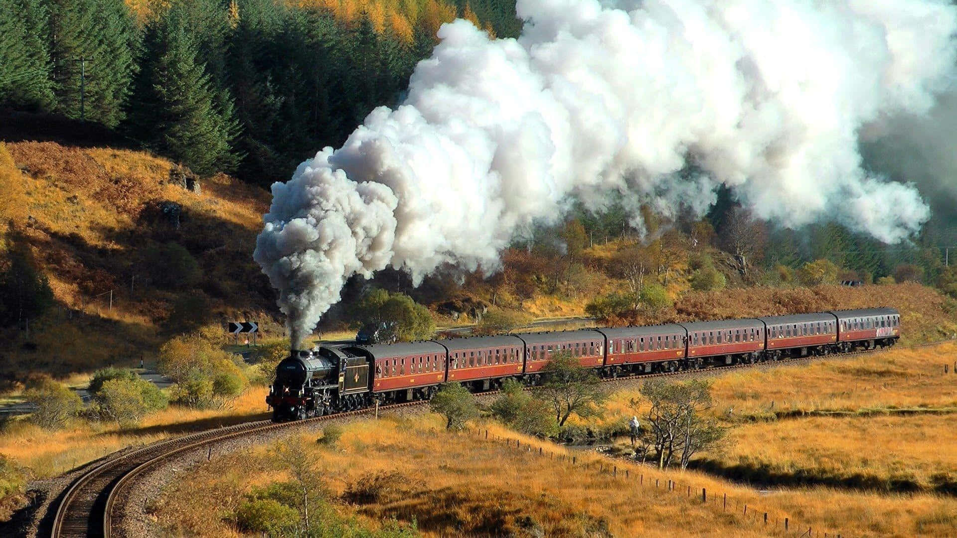 Hogwarts Express 桌布 壁紙 — 一輛復古蒸汽火車在穿過金黃色秋日山谷時噴出濃厚白煙，山谷兩旁是常綠森林。