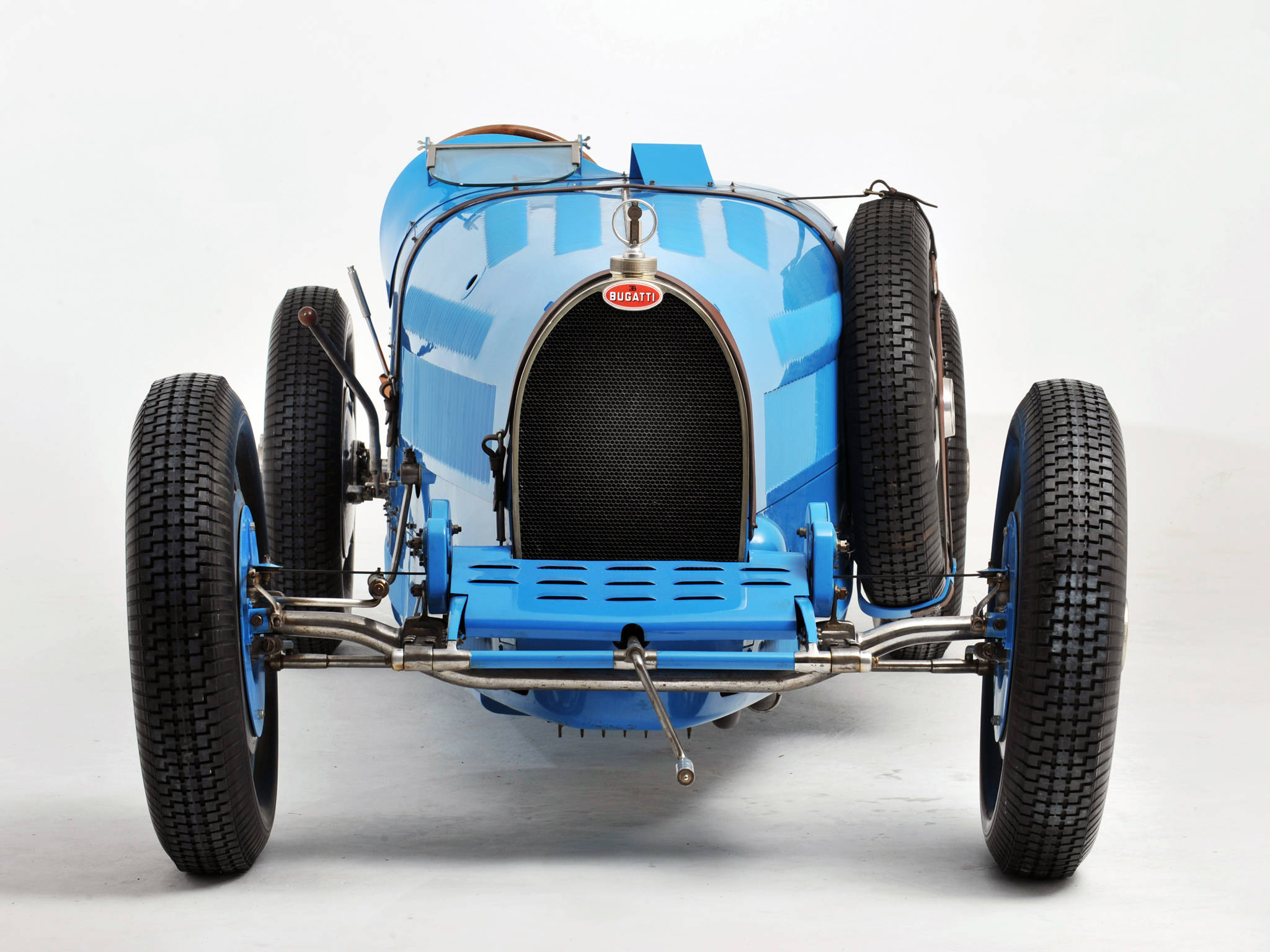 bugatti iPhone 桌布 壁紙 — 一輛復古藍色Bugatti賽車，帶有外露底盤和備用輪胎，在純白色工作室背景前蓄勢待發。