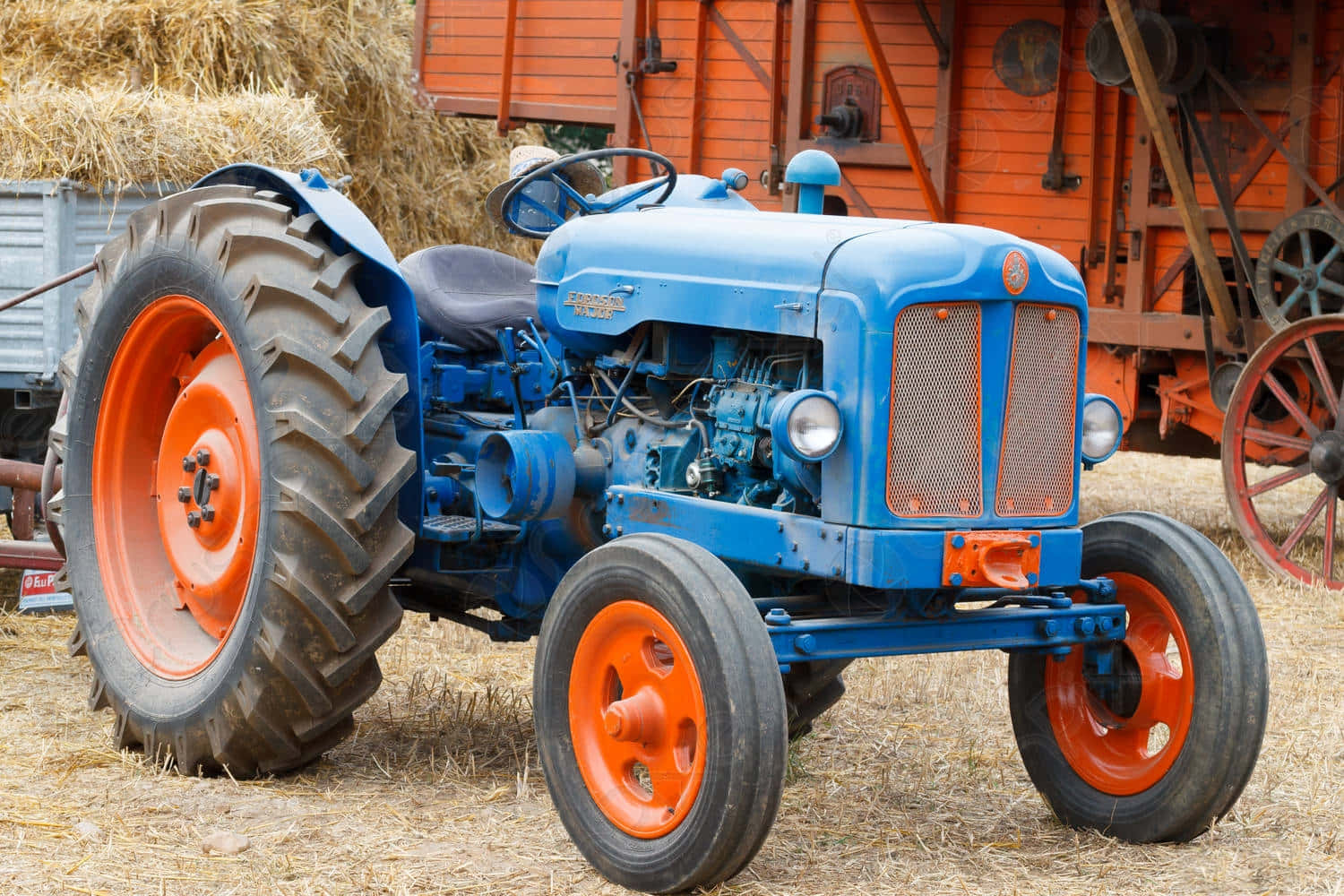 Tractor 桌布 壁紙 — 一輛復古藍色拖拉機帶橙色輪子停在乾草上，旁邊是紅色穀倉和乾草捆。