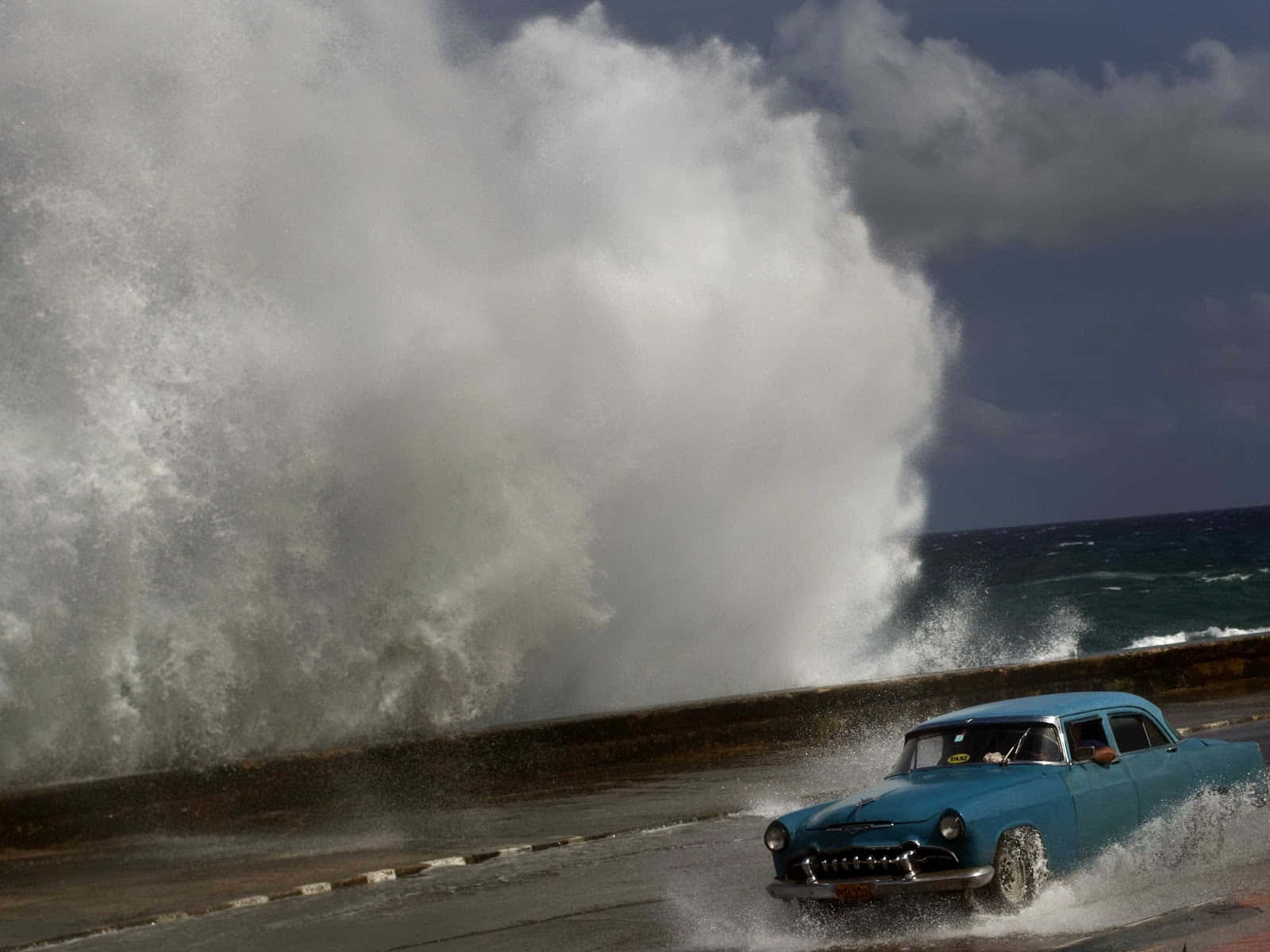 Hurricane 桌布 壁紙 — 一輛復古藍色汽車在暴風雨天空下濺起水花行駛，身後有巨大的海浪正在破碎。