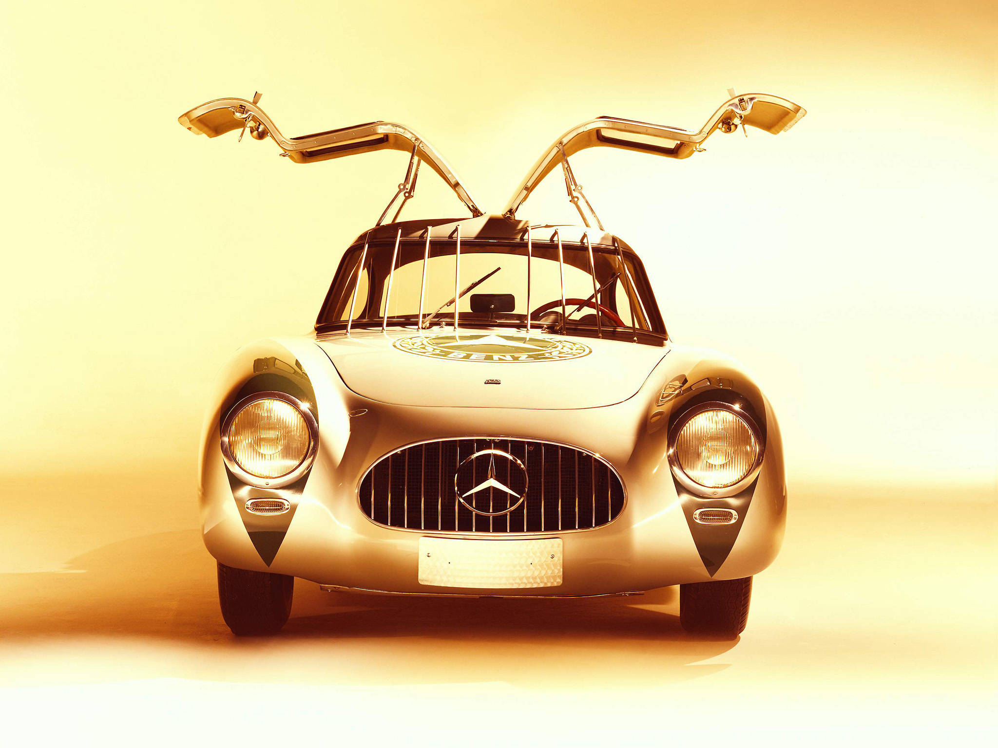 HD mercedes 桌布 壁紙 — 一輛復古賓士300 SL，鷗翼車門打開，沐浴在溫暖的金色工作室燈光中。