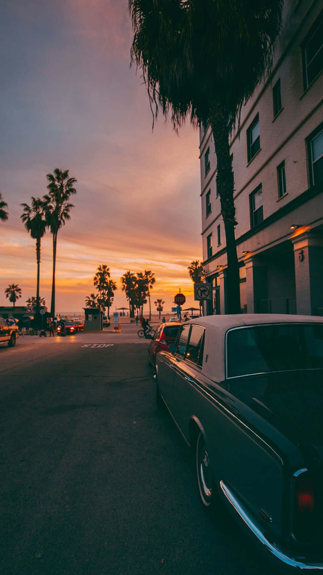 California Aesthetic 桌布 壁紙 — 一輛復古車停在棕櫚樹成蔭的街道上，建築物後方的天空閃耀著夕陽色調。