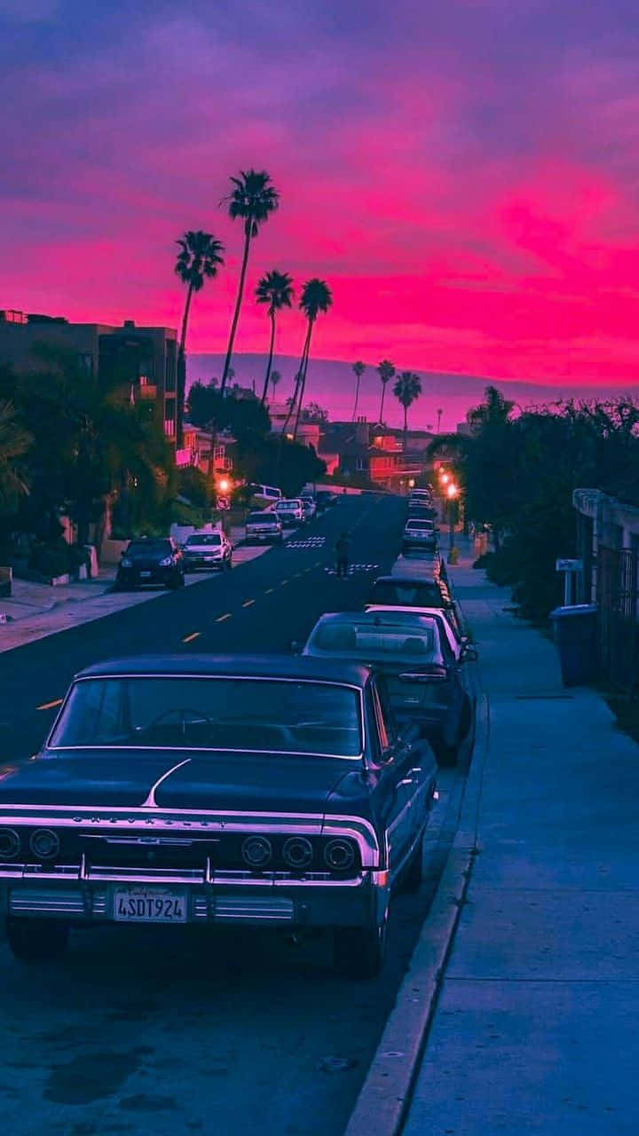 Aesthetic Car 桌布 壁紙 — 一輛復古車停在街上，天空是充滿活力的粉紅色和紫色日落，有棕櫚樹。