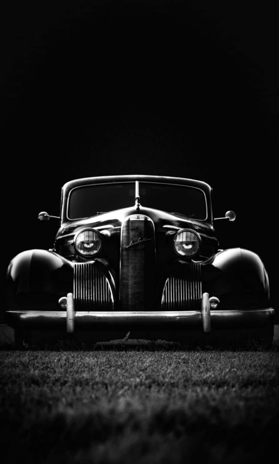 Vintage Black And White 桌布 壁紙 — 一輛復古車的前格柵在戲劇性的聚光燈下閃閃發光，背景漆黑，前景有草。