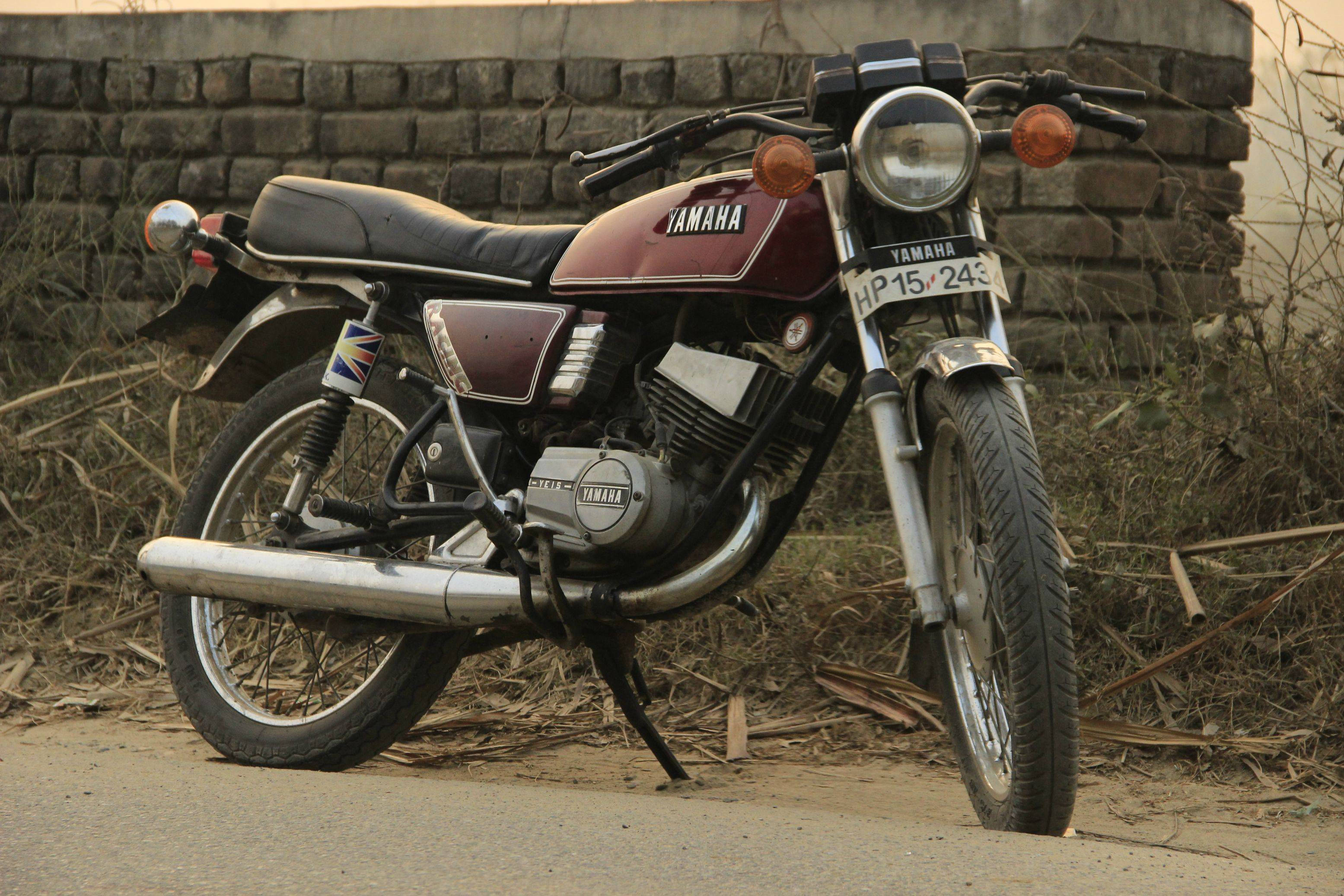 Rx100 桌布 壁紙 — 一輛復古酒紅色Yamaha機車停放在塵土飛揚的路邊，背景是風化的磚牆。