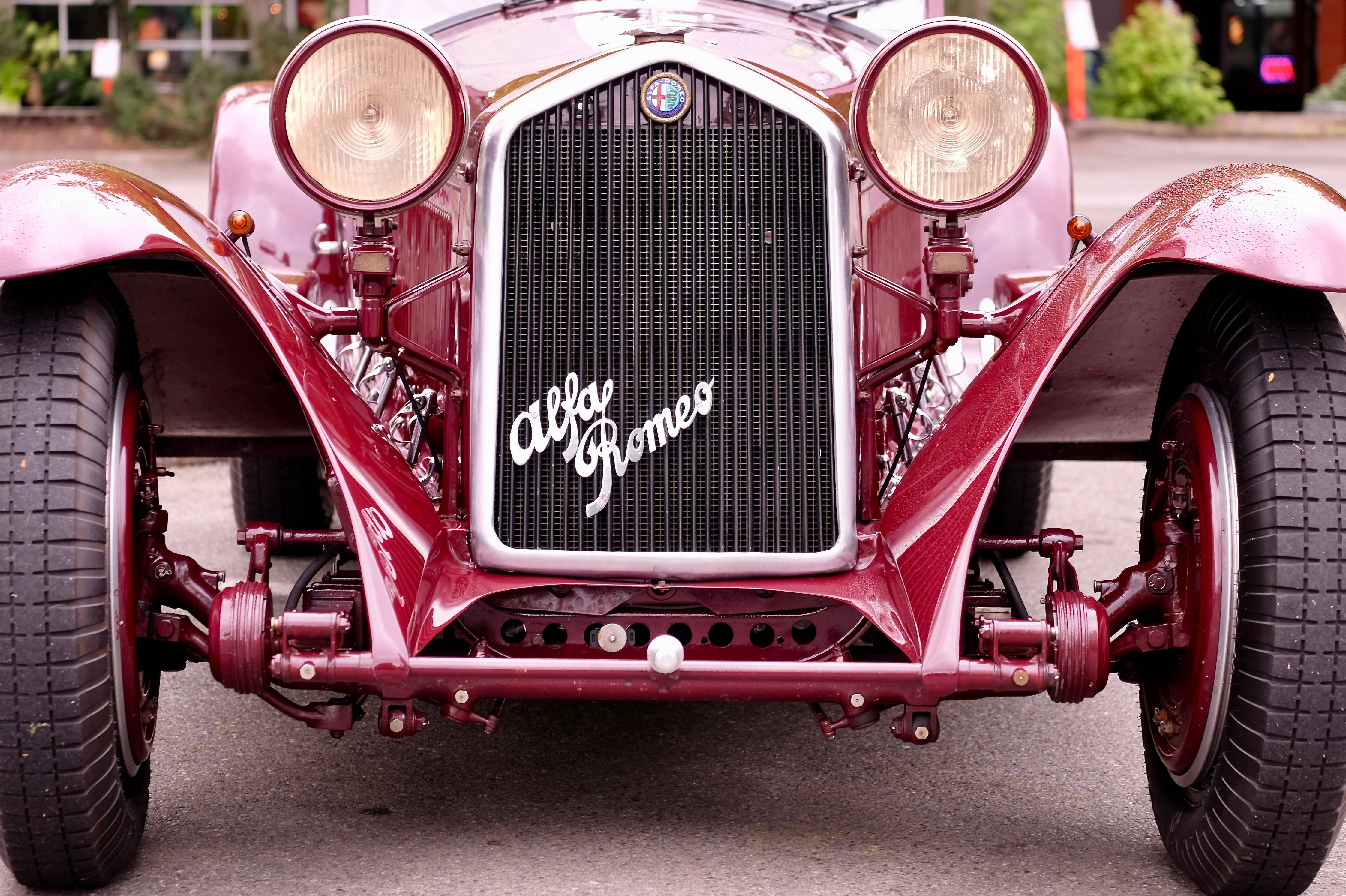 Alfa Romeo 桌布 壁紙 — 一輛復古酒紅色愛快羅密歐汽車的特寫，展示其標誌性格柵和圓形頭燈。