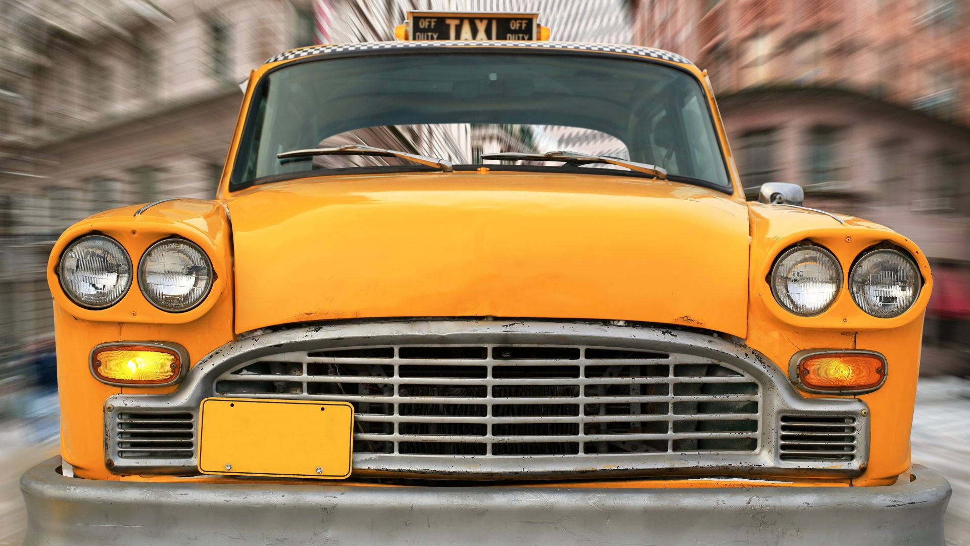 taxi 桌布 壁紙 — 一輛復古黃色的士在城市街道上疾馳，背景建築物呈現動態模糊效果。