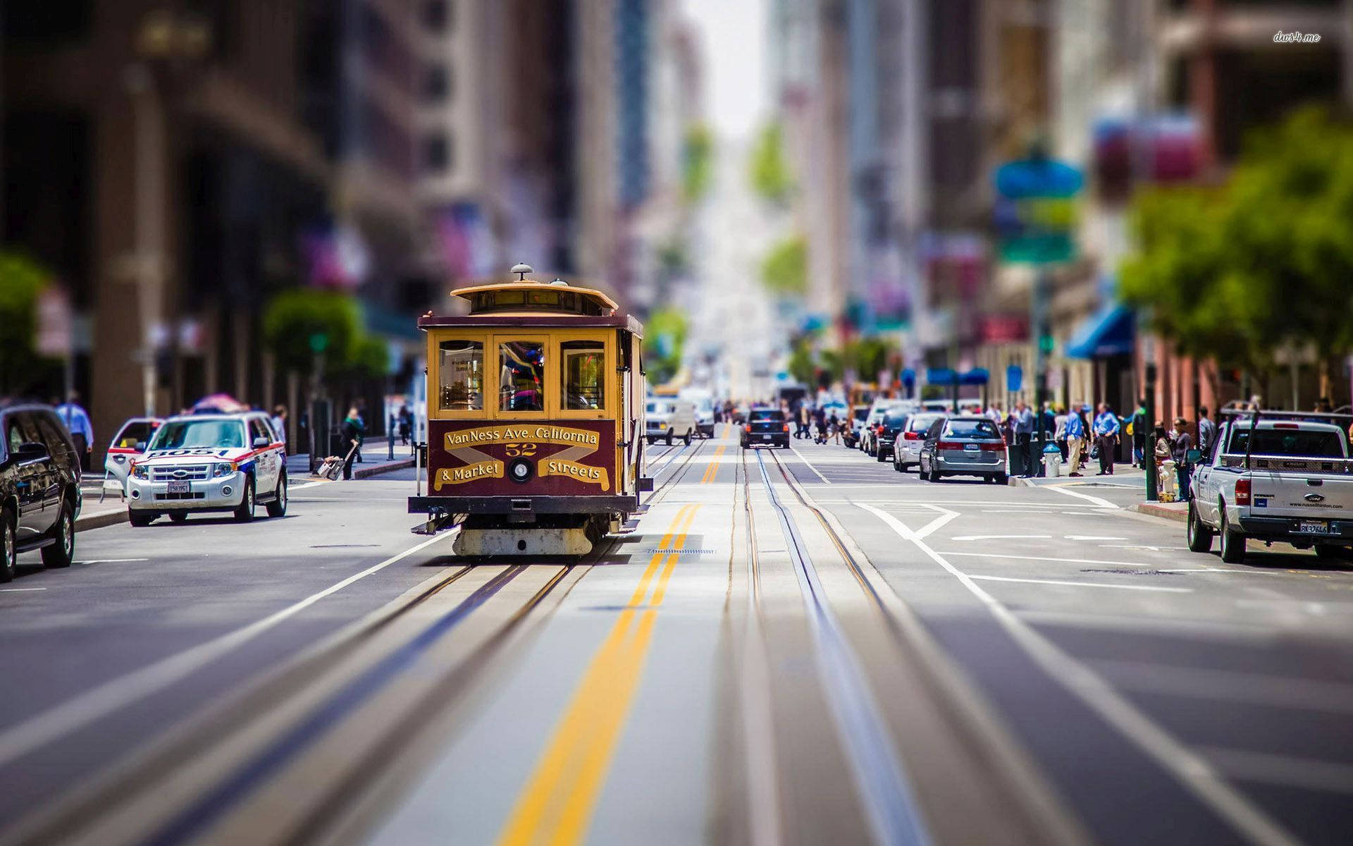 transportation 桌布 壁紙 — 一輛復古黃色纜車沿著陽光明媚的舊金山街道滑行，背景是模糊的汽車和行人。