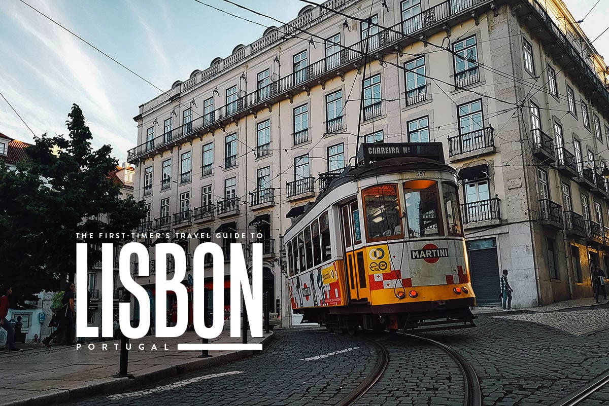 Portugal 桌布 壁紙 — 一輛復古黃色里斯本電車沿著鵝卵石街道蜿蜒而行，經過歷史悠久的白色建築，頭頂是清澈的藍天。