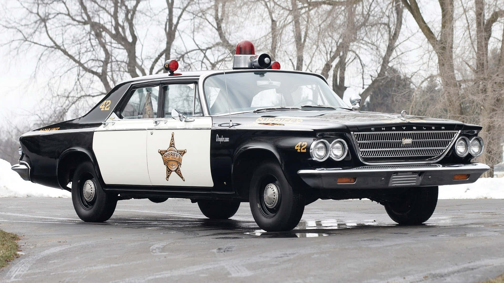 Law Enforcement 桌布 壁紙 — 一輛復古黑白克萊斯勒警長車，帶有紅色燈光，停在被光禿樹木包圍的雪路上。