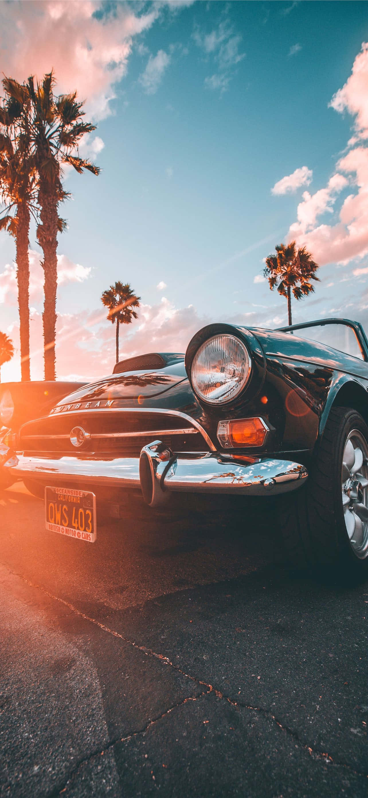 California Aesthetic 桌布 壁紙 — 一輛復古黑色敞篷跑車在溫暖的日落天空下閃閃發光，周圍環繞著高大的棕櫚樹。