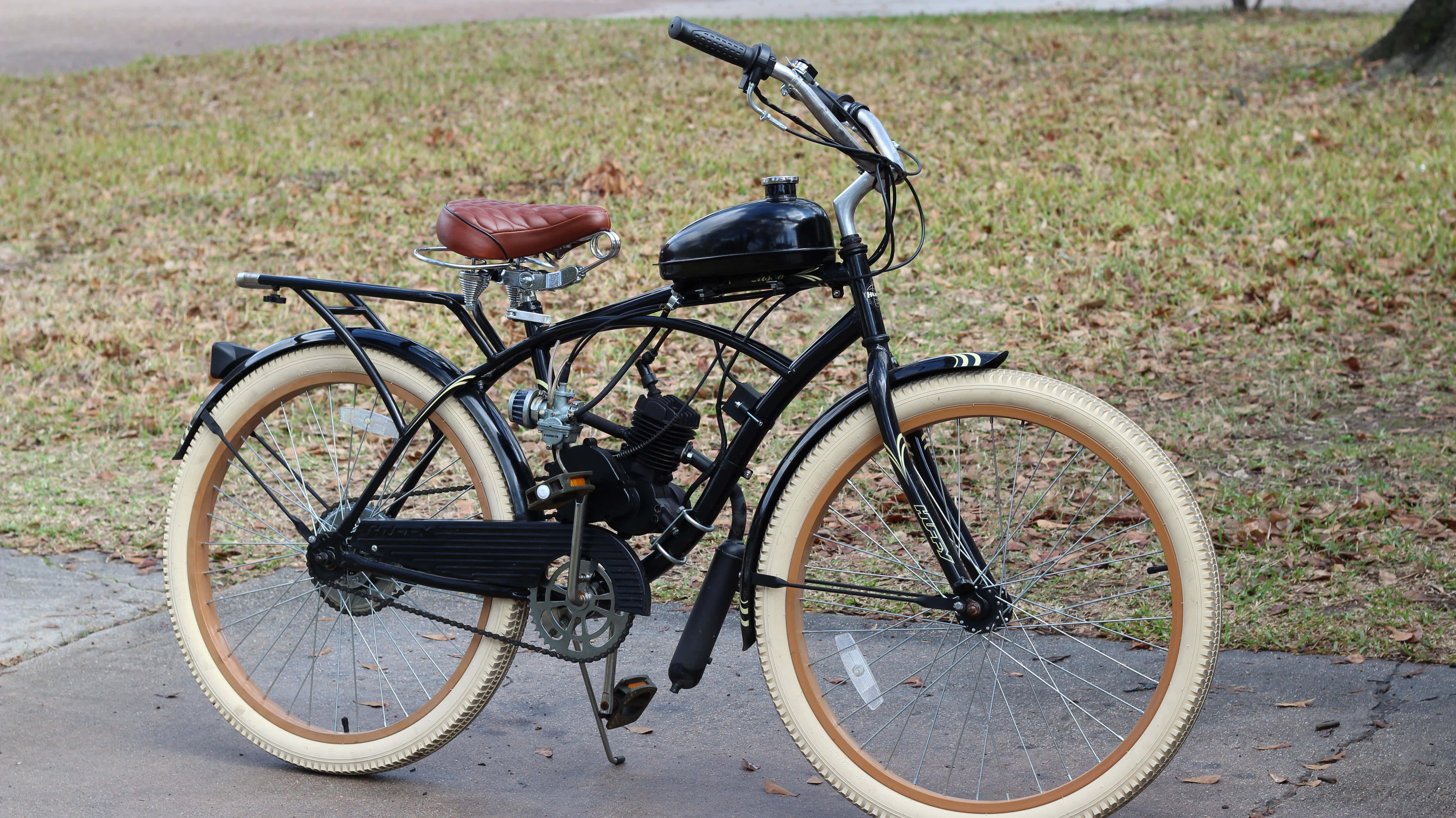 Beach Cruiser 桌布 壁紙 — 一輛復古黑色機動自行車，配奶油色輪胎和紅色座椅，停放在草地旁的人行道上。