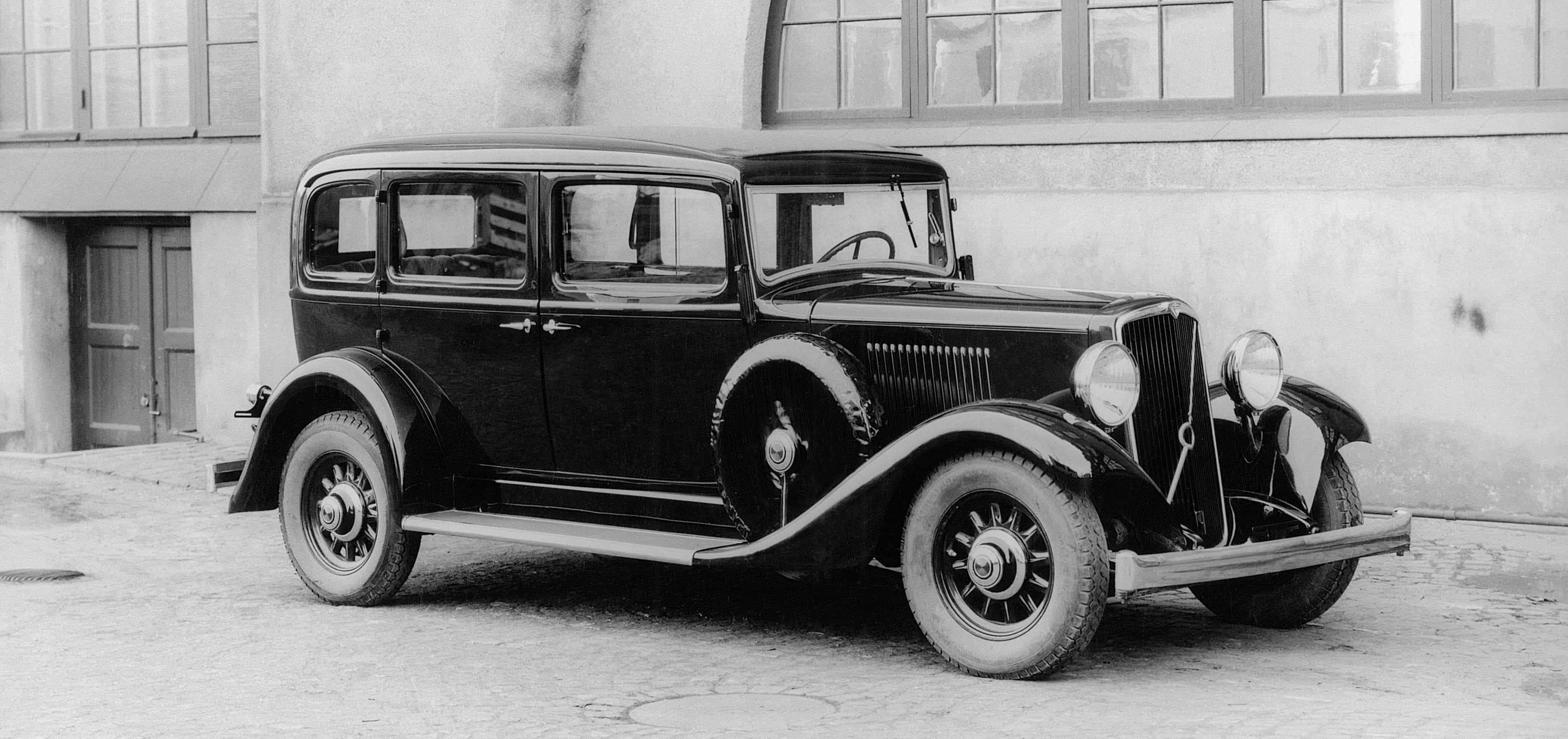 Black And White Vintage Car 桌布 壁紙 — 一輛復古黑色轎車停在一棟有大窗戶和門的建築物外面。