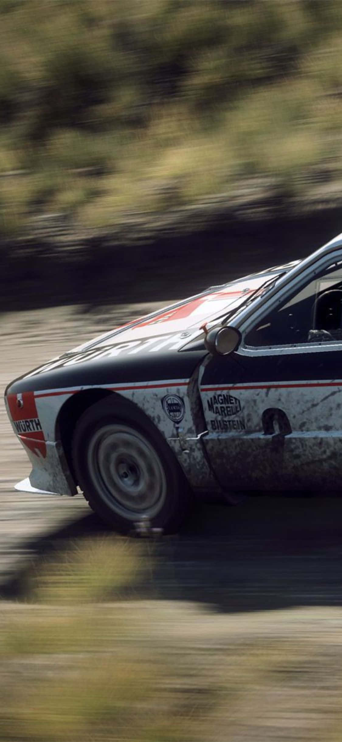 iPhone Xs Dirt Rally 桌布 壁紙 — 一輛拉力賽車在森林中的泥路上高速行駛，動態模糊強調了高速。