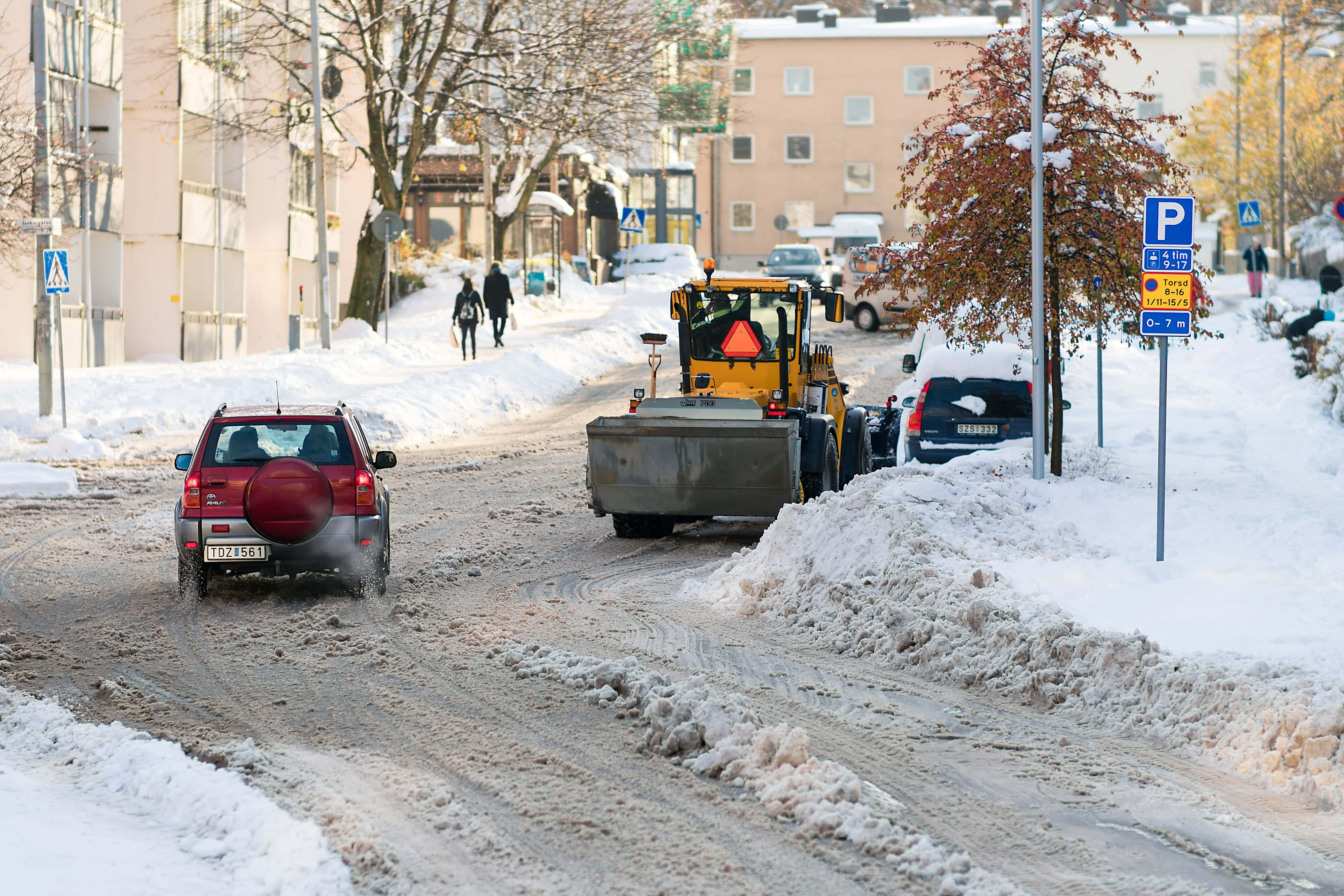 Snowplow 桌布 壁紙 — 一輛掃雪車正在清理積雪的城市街道，汽車和行人應對冬季條件。