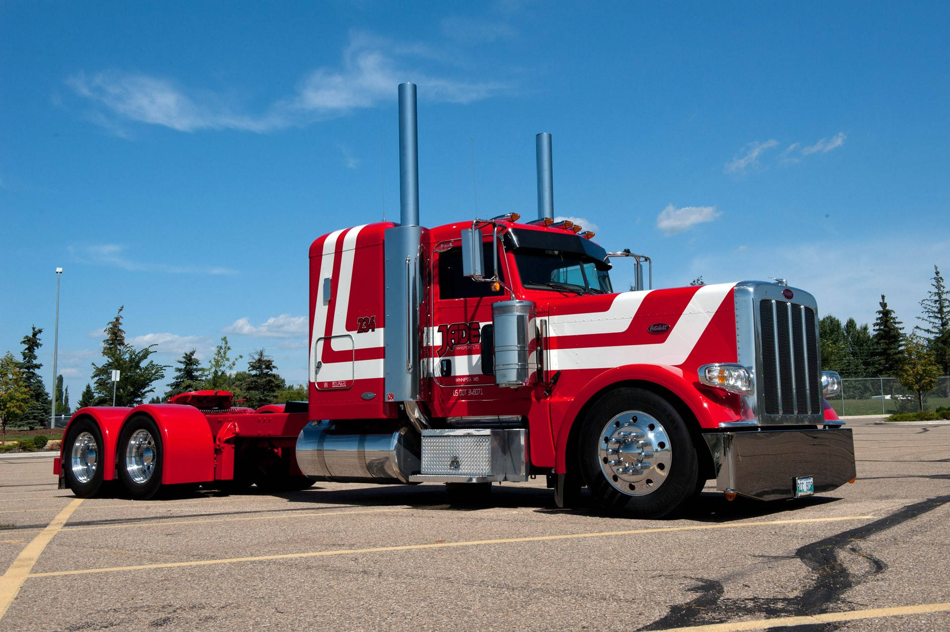 Peterbilt 桌布 壁紙 — 一輛搶眼的紅白色Peterbilt半掛卡車，帶有鍍鉻裝飾，停放在陽光普照的停車場，背景是清澈的藍天。