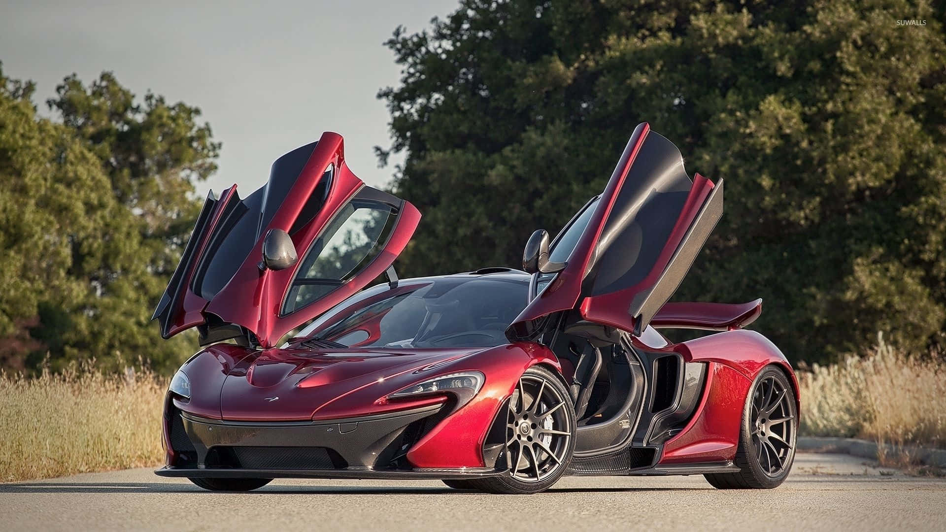 Cool Car 桌布 壁紙 — 一輛搶眼的紅色McLaren跑車，鷗翼車門打開，停在鋪砌的道路上，周圍是綠樹和乾草，天空明亮。