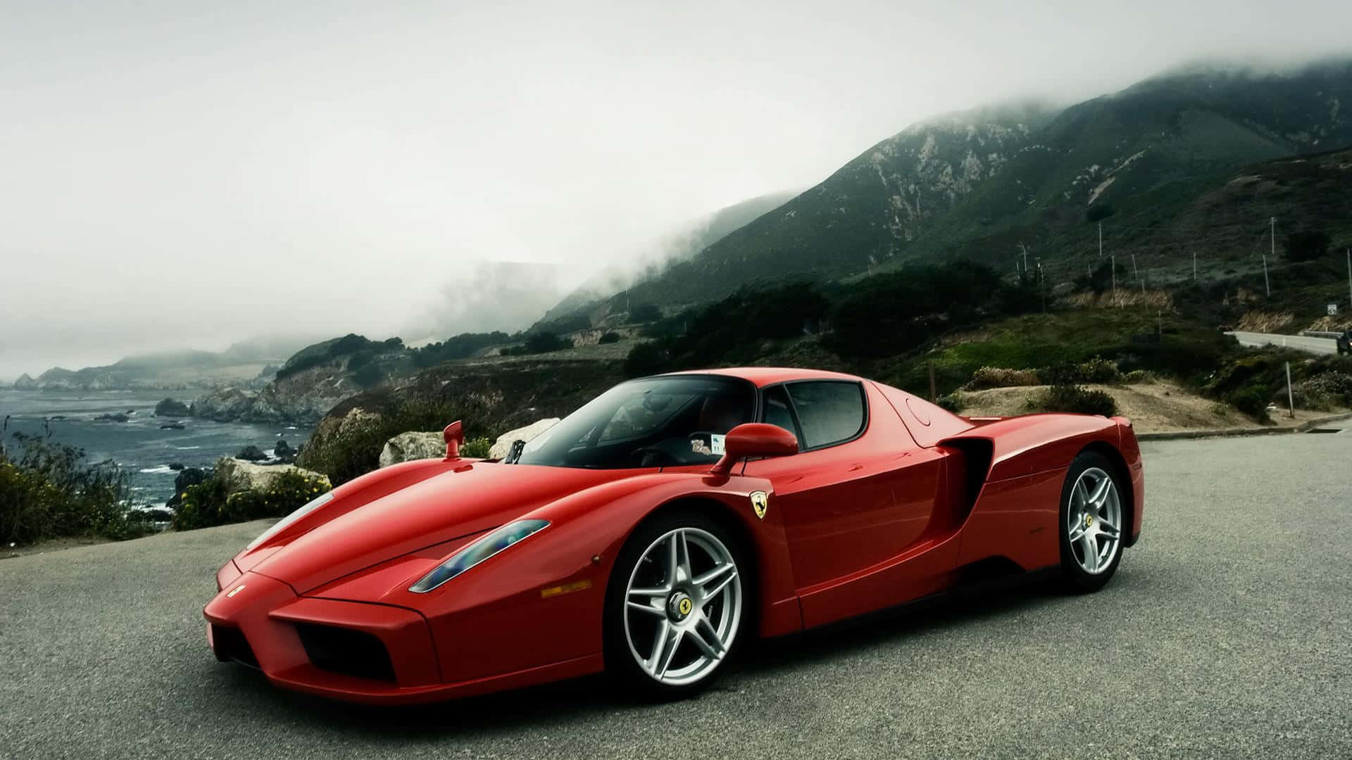 汽車 4K 桌布 壁紙 — 一輛搶眼的紅色法拉利Enzo停泊在沿海公路上，背景是霧氣繚繞的山巒和海洋。
