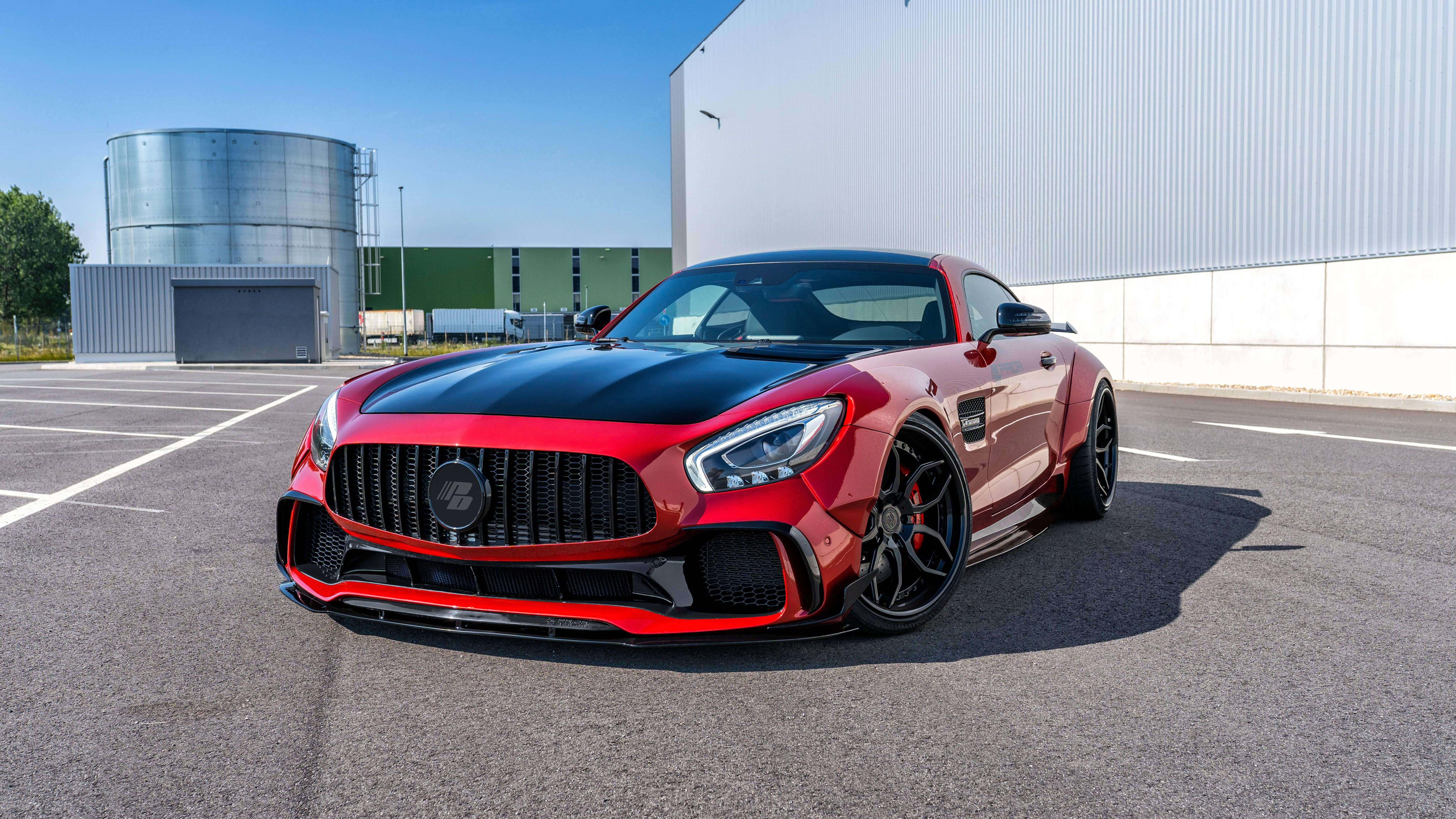 高畫質 賓士 桌布 壁紙 — 一輛搶眼的紅黑色 Mercedes-AMG GT R 跑車停泊在陽光普照的工業用地，背景有一個大型銀色儲罐和白色建築物。