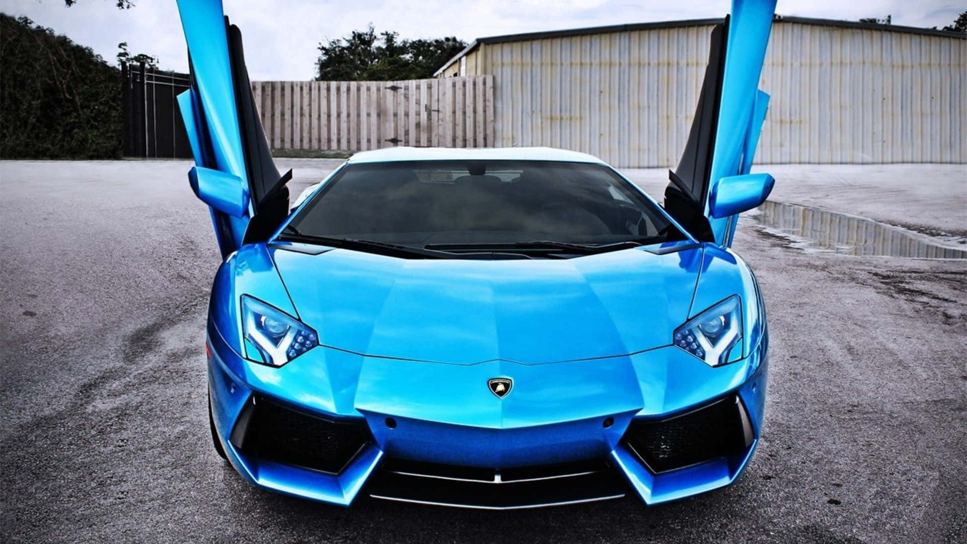 Lamborghini Aventador 桌布 壁紙 — 一輛搶眼的藍色藍寶堅尼Aventador，剪刀門打開，停在混凝土場地上，背景是飽經風霜的金屬建築。