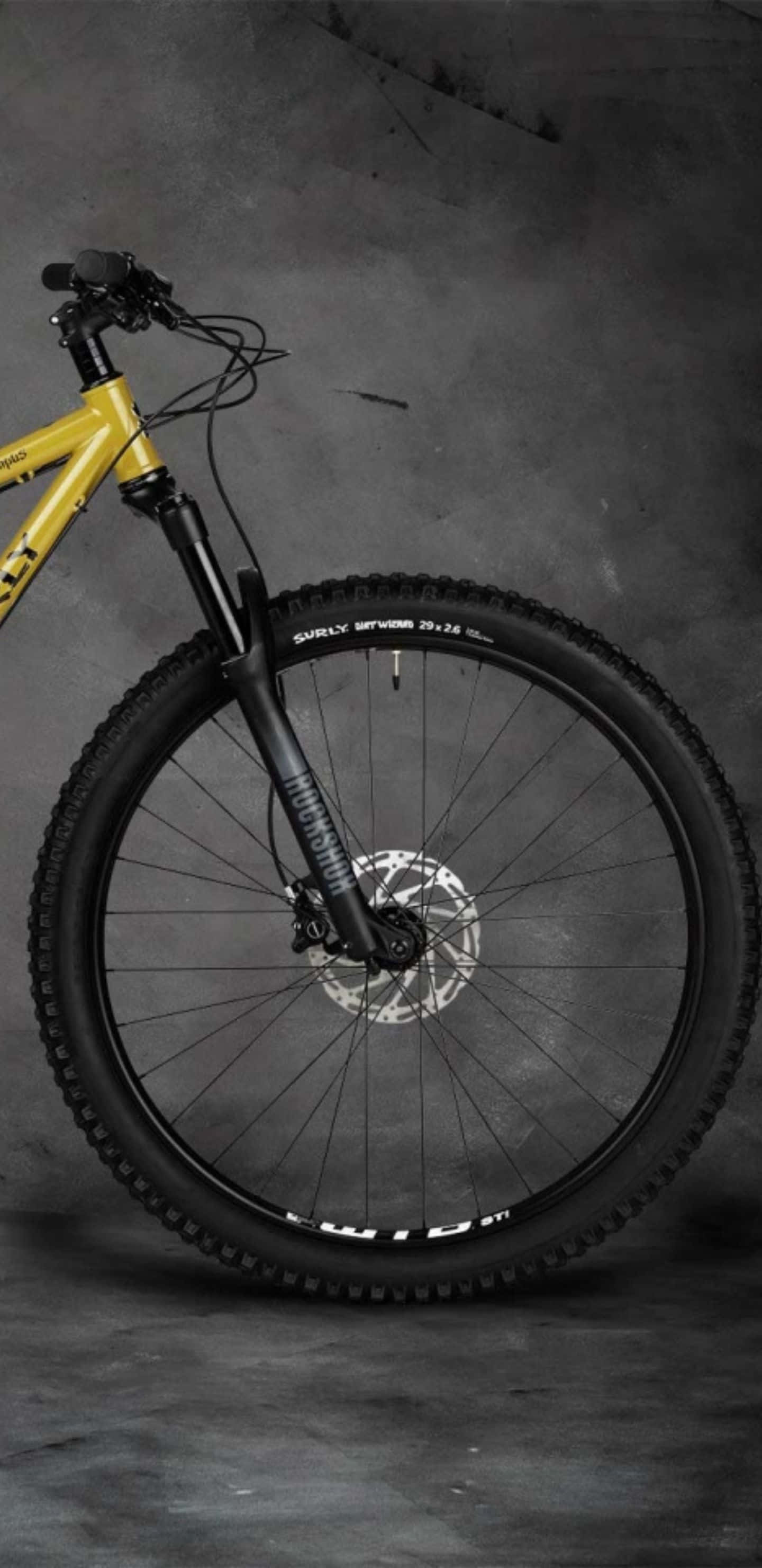 Pixel 3xl Bikes 桌布 壁紙 — 一輛搶眼的黃色登山車，配備黑色前叉和防滑輪胎，矗立在紋理灰色工作室背景前。