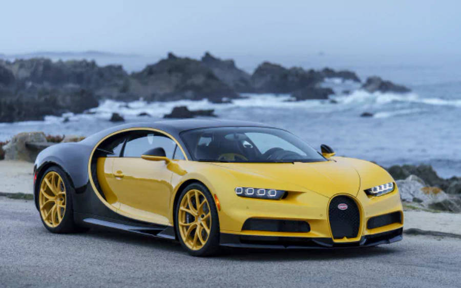 4K 桌布 壁紙 — 一輛搶眼的黃黑 Bugatti Chiron 停泊在沿海公路上，背後有洶湧的海浪和岩石峭壁。