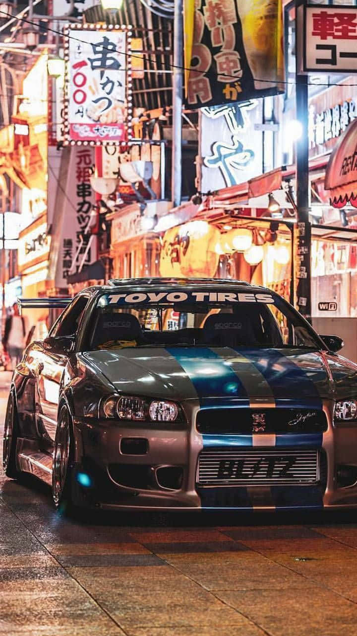 日產 桌布 壁紙 — 一輛改裝的銀色跑車帶有藍色條紋，夜晚停在潮濕的霓虹燈日本街道上。