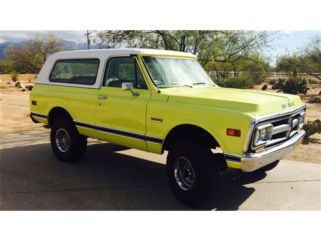 Gmc Jimmy 桌布 壁紙 — 一輛明亮的萊姆綠色經典雪佛蘭K5 Blazer，白色車頂，停在鋪砌的車道上，背景是沙漠景觀，有仙人掌和遠處的山脈，天空清澈湛藍。
