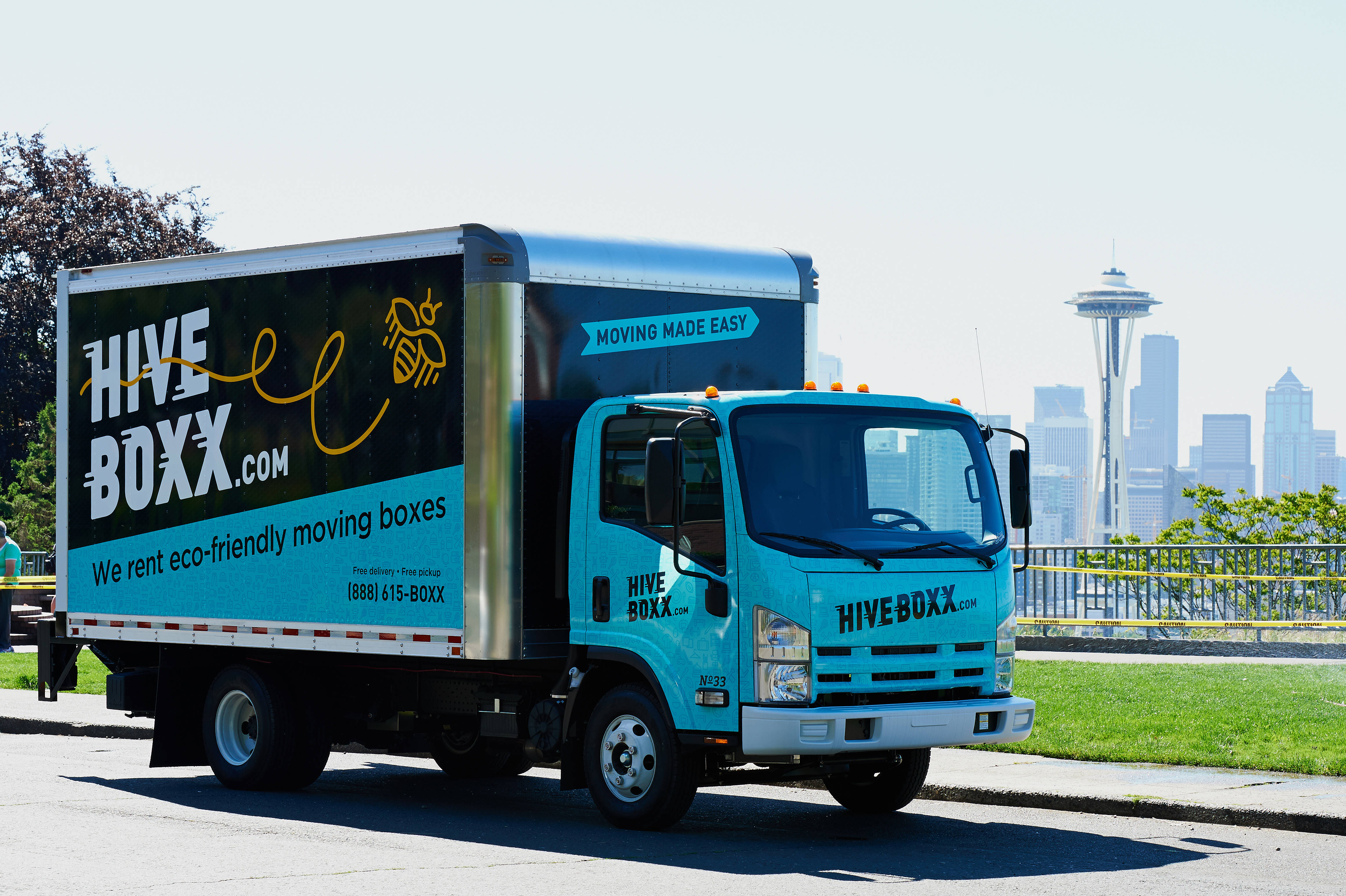 Truck 桌布 壁紙 — 一輛明亮的藍綠色Hive Boxx搬家貨車停泊在陽光明媚的街道上，背景是西雅圖的太空針塔和天際線。
