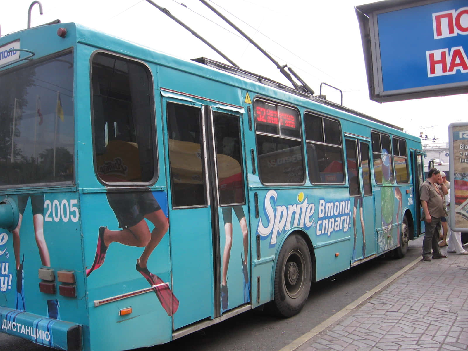 Transport 桌布 壁紙 — 一輛明亮的藍綠色無軌電車，帶有大型雪碧廣告和2005年，停靠在車站，附近有人。