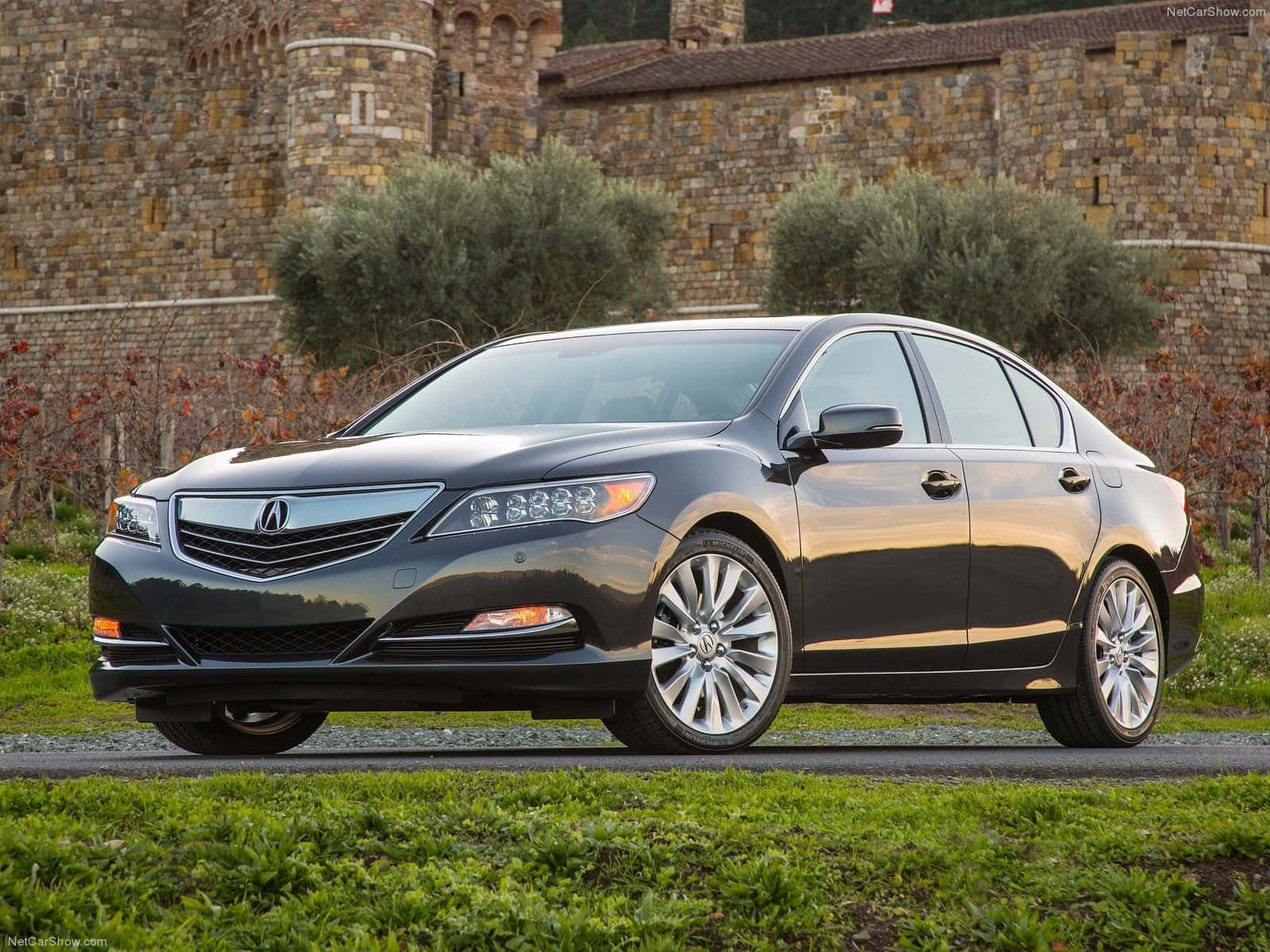 Acura Rlx 桌布 壁紙 — 一輛時尚深灰色Acura轎車停在碎石路上，前方是一座鄉村風格的石城堡，周圍有橄欖樹和秋天的樹葉。