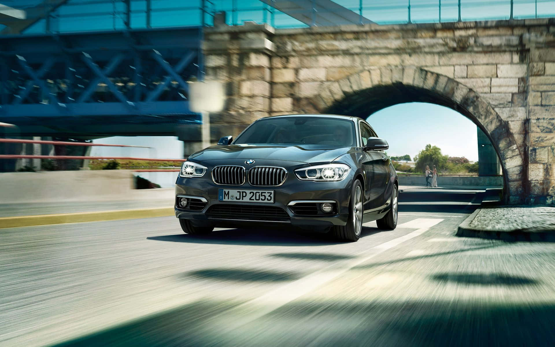 Bmw 1 Series 桌布 壁紙 — 一輛時尚深灰色寶馬轎跑車在石拱橋下高速行駛，路上帶有動態模糊效果。