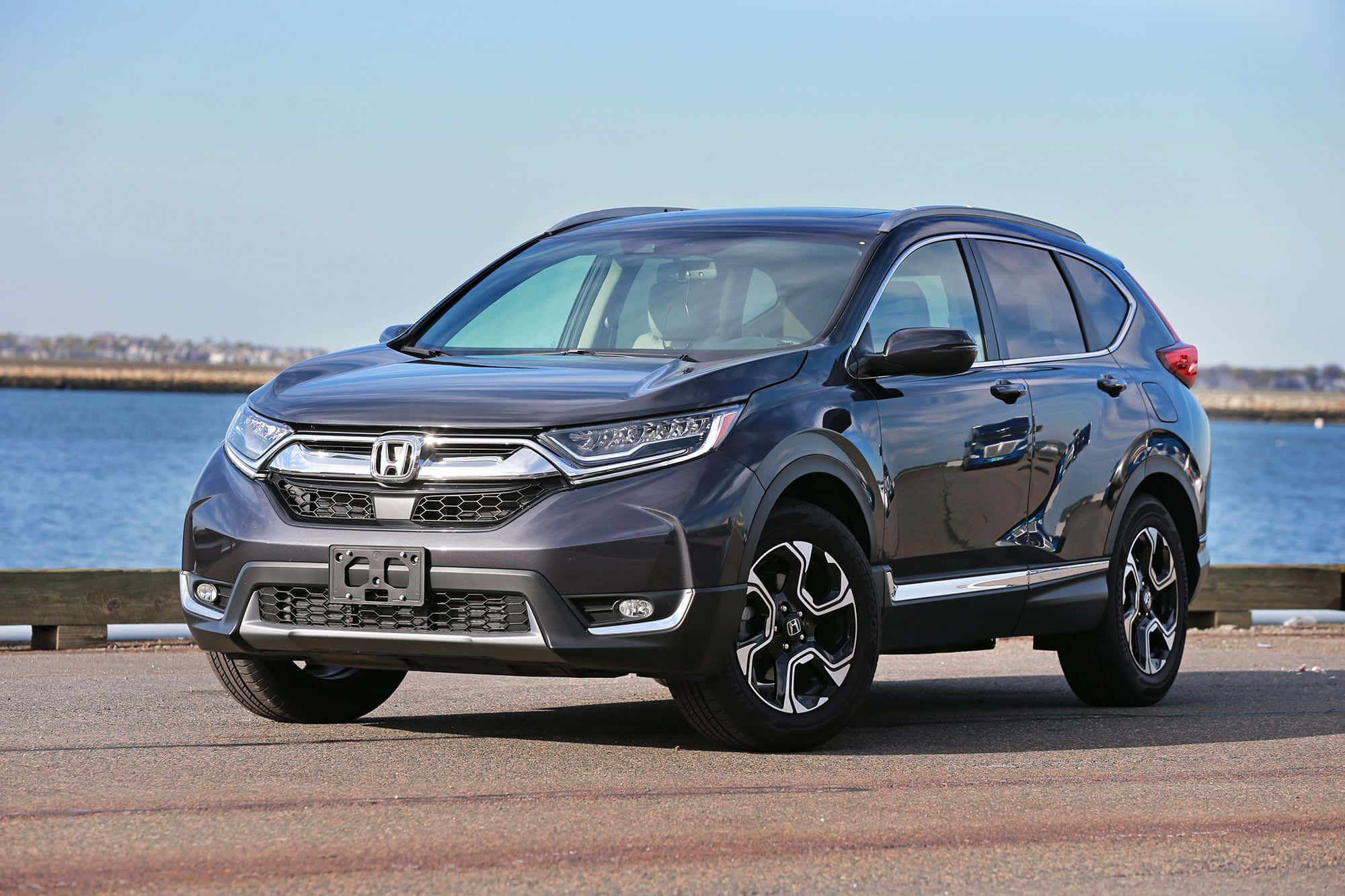 Honda Cr-v 桌布 壁紙 — 一輛時尚深灰色本田CR-V SUV停泊在海濱，平靜的藍色海水和遠處的海岸線，天空晴朗。