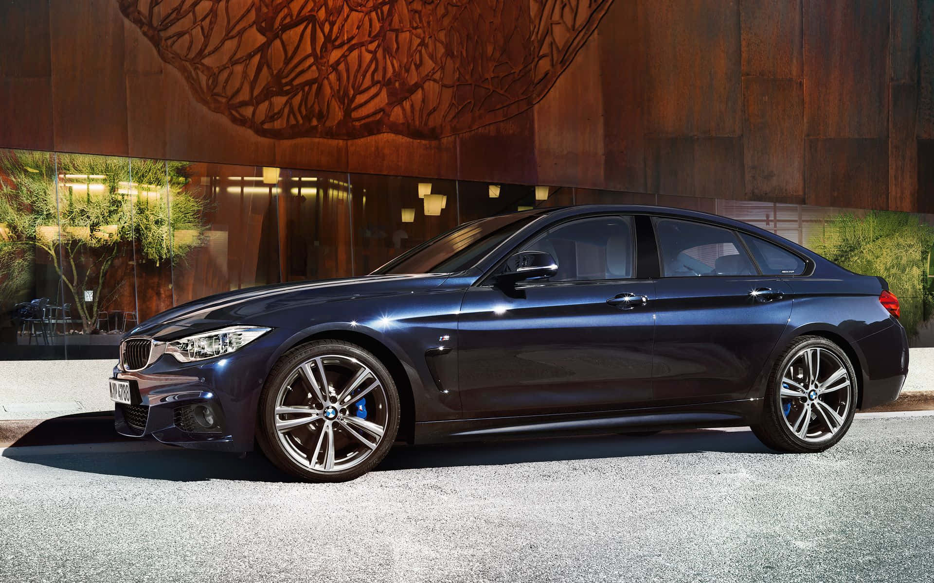 Bmw 4 Series 桌布 壁紙 — 一輛時尚深藍色寶馬轎車停在碎石路上，前方是現代建築，外牆為木質並配以玻璃窗。