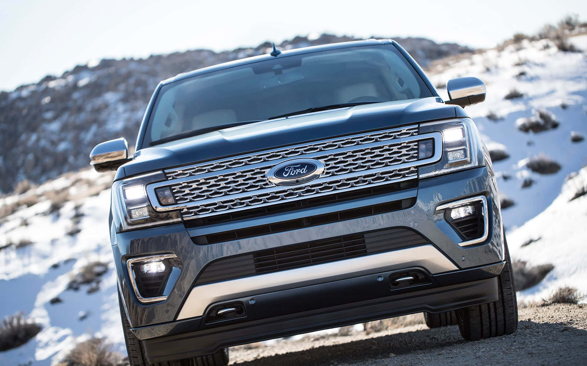 Ford Expedition 桌布 壁紙 — 一輛時尚深藍色福特Explorer SUV停放在積雪的山路上，背景是崎嶇的地形。